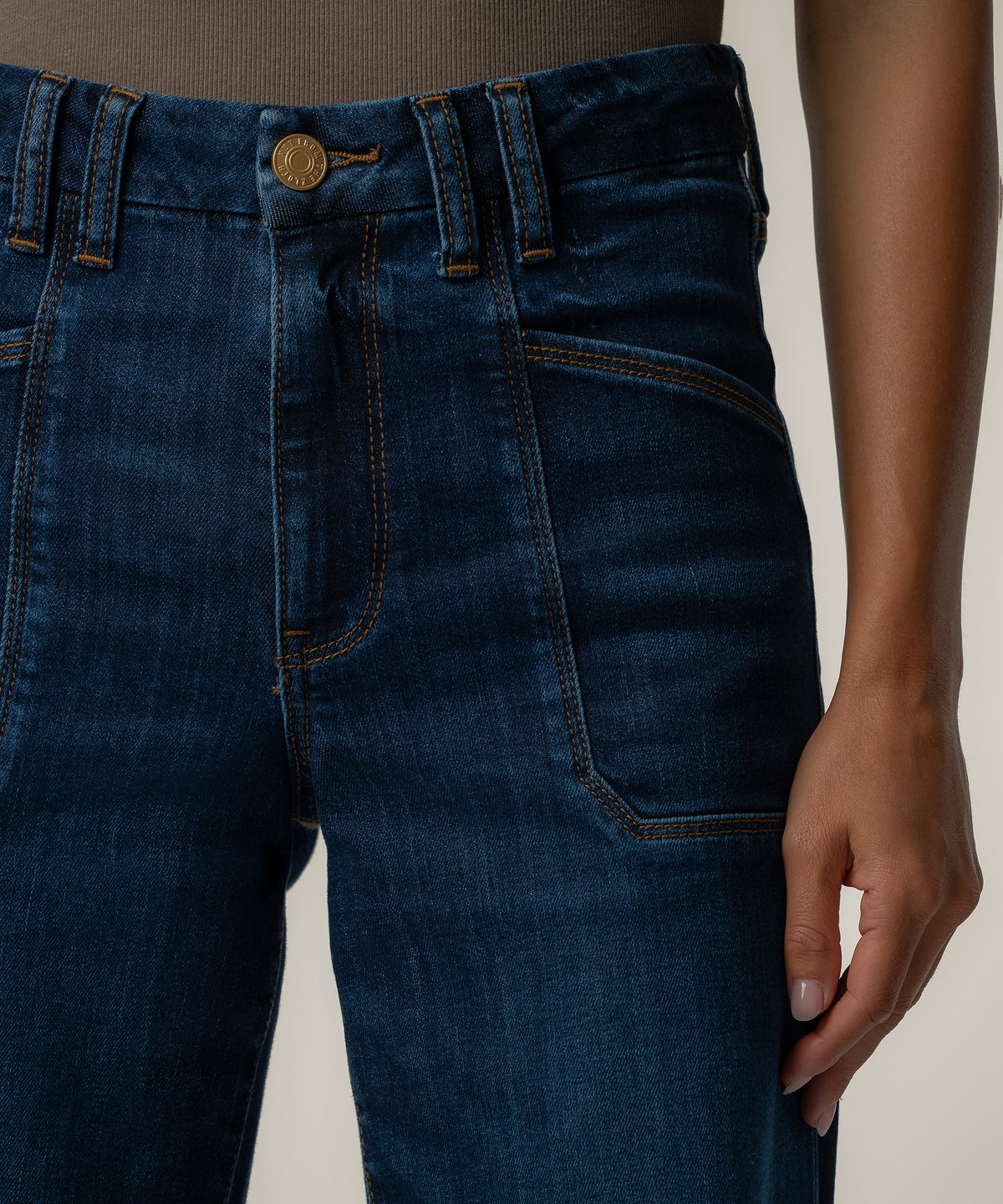 Close-up of a person wearing dark blue wide-leg jeans with a gold button, tan topstitching, and large front patch pockets.