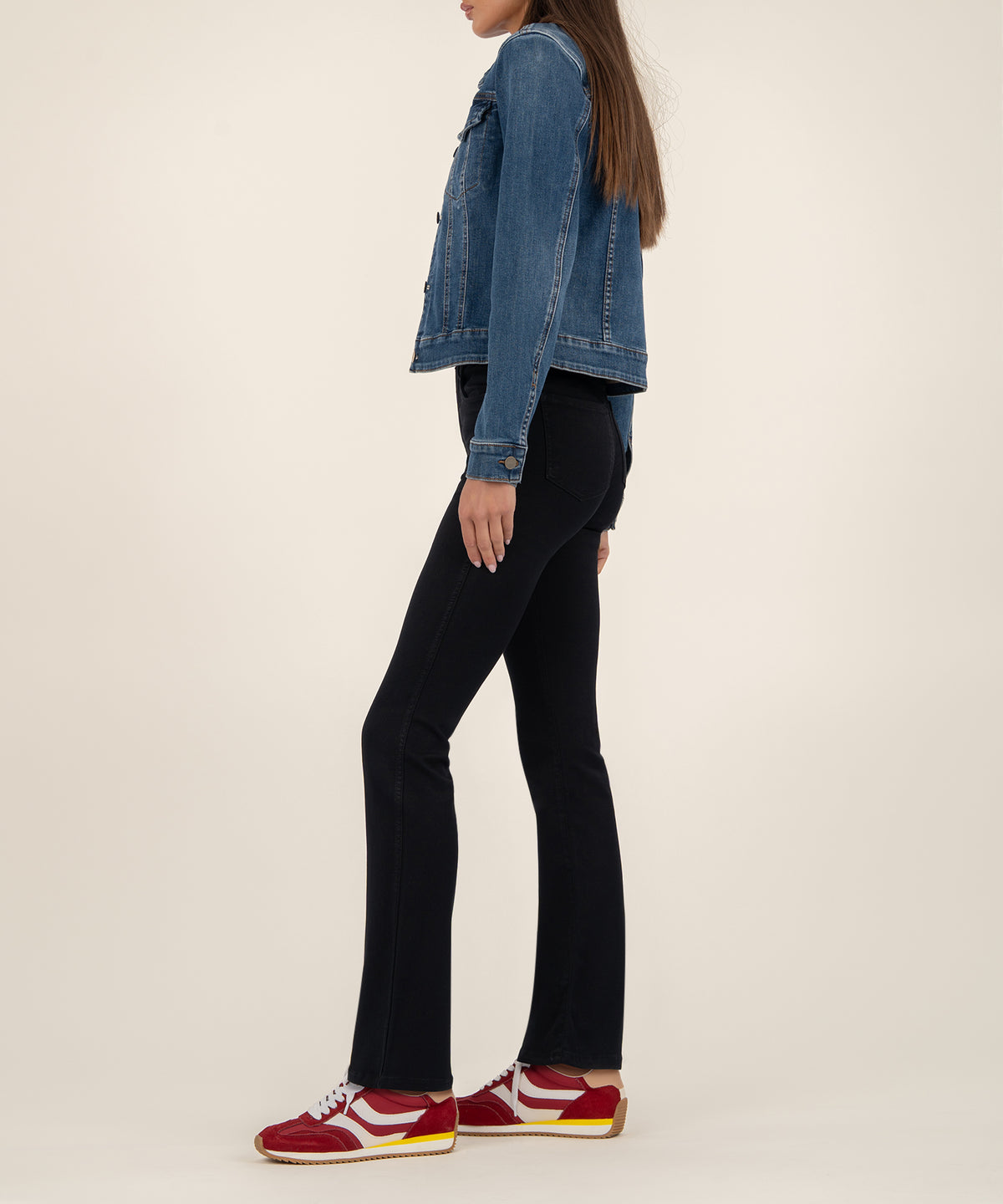 Woman wearing a cropped blue denim jacket with button front and long sleeves, styled with black flared jeans and red sneakers