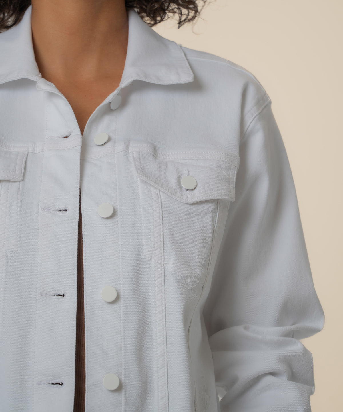 White button-front jacket with collar, chest pockets, and long sleeves worn by model with dark curly hair.