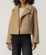 A person wears a cropped tan wool-style jacket with wide lapels over a white top and black jeans.