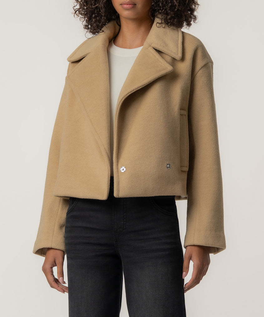 A person wears a cropped tan wool-style jacket with wide lapels over a white top and black jeans.