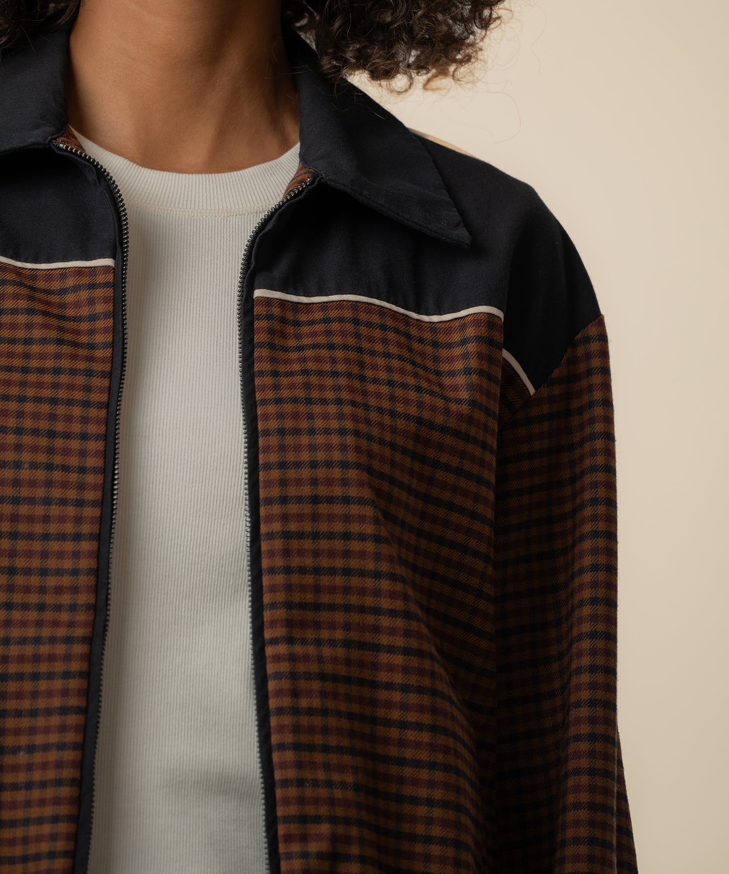 Black and brown houndstooth track jacket with collar and zip front, worn over white ribbed shirt.