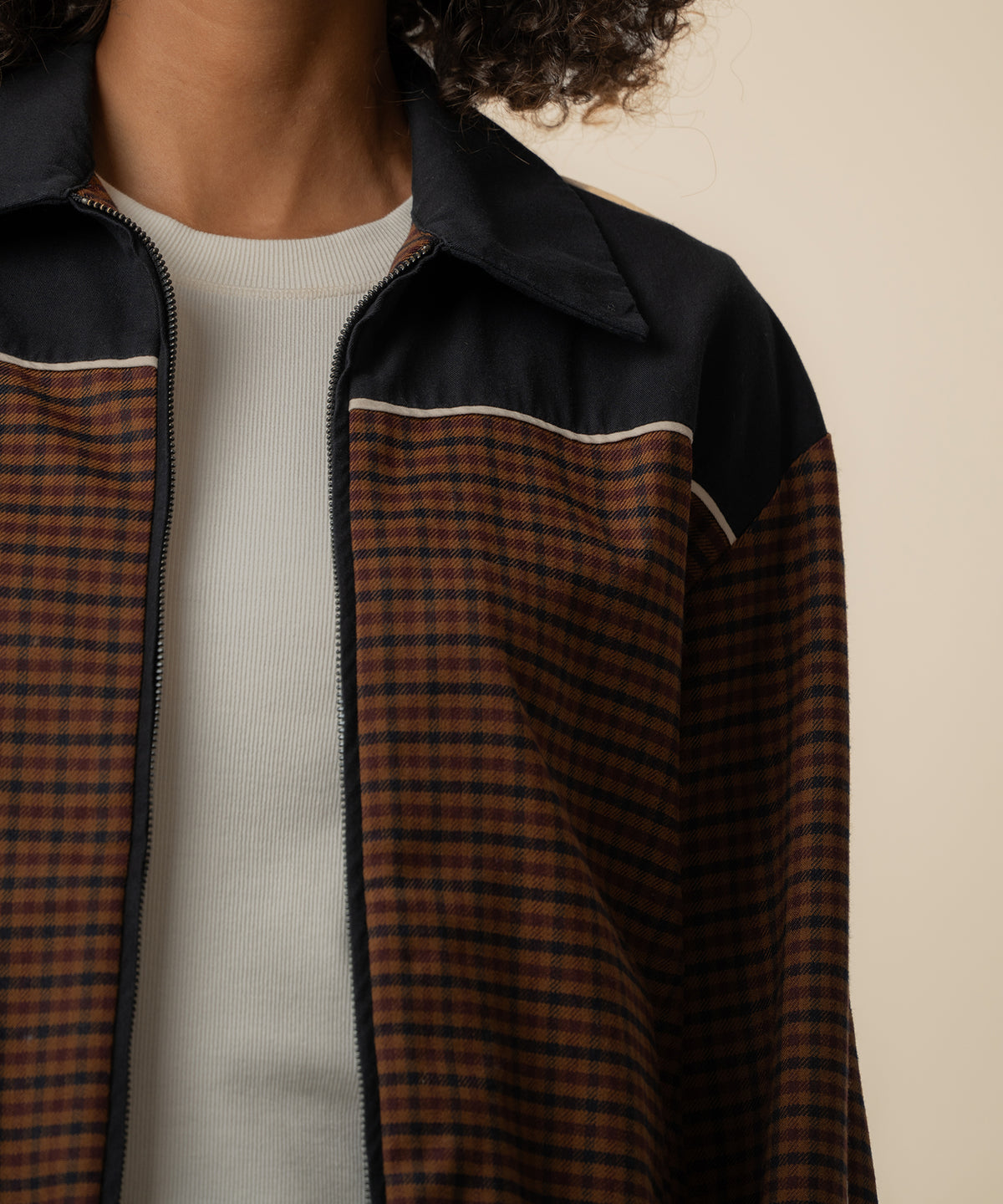 Black and brown houndstooth track jacket with collar and zip front, worn over white ribbed shirt.