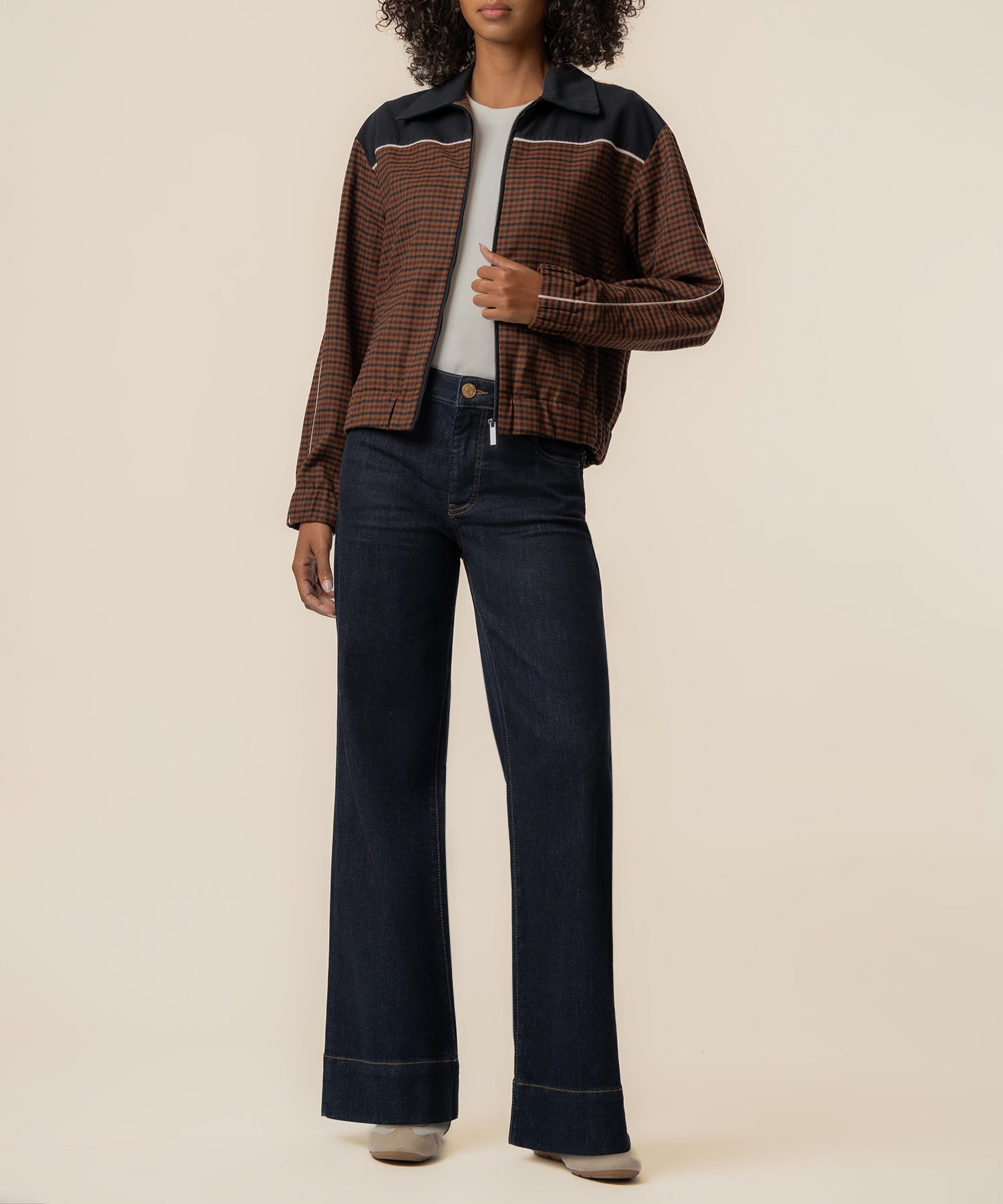 Black and brown checked track jacket with white stripe trim and collar, worn with dark jeans.