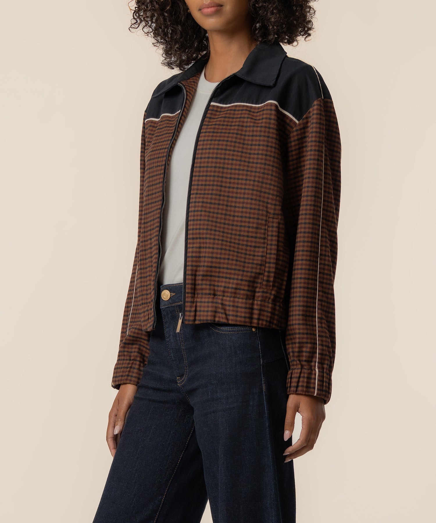 Black and brown gingham track jacket with contrast collar and piping worn over white tee and dark jeans.