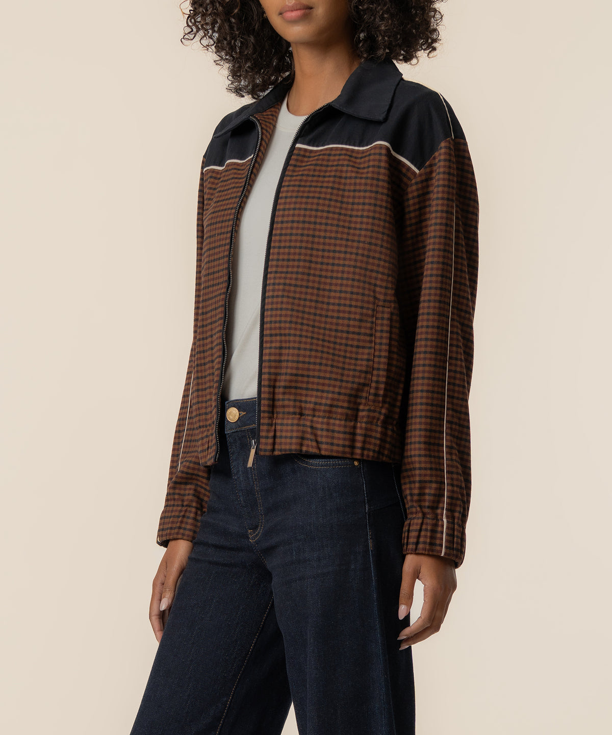 Black and brown gingham track jacket with contrast collar and piping worn over white tee and dark jeans.