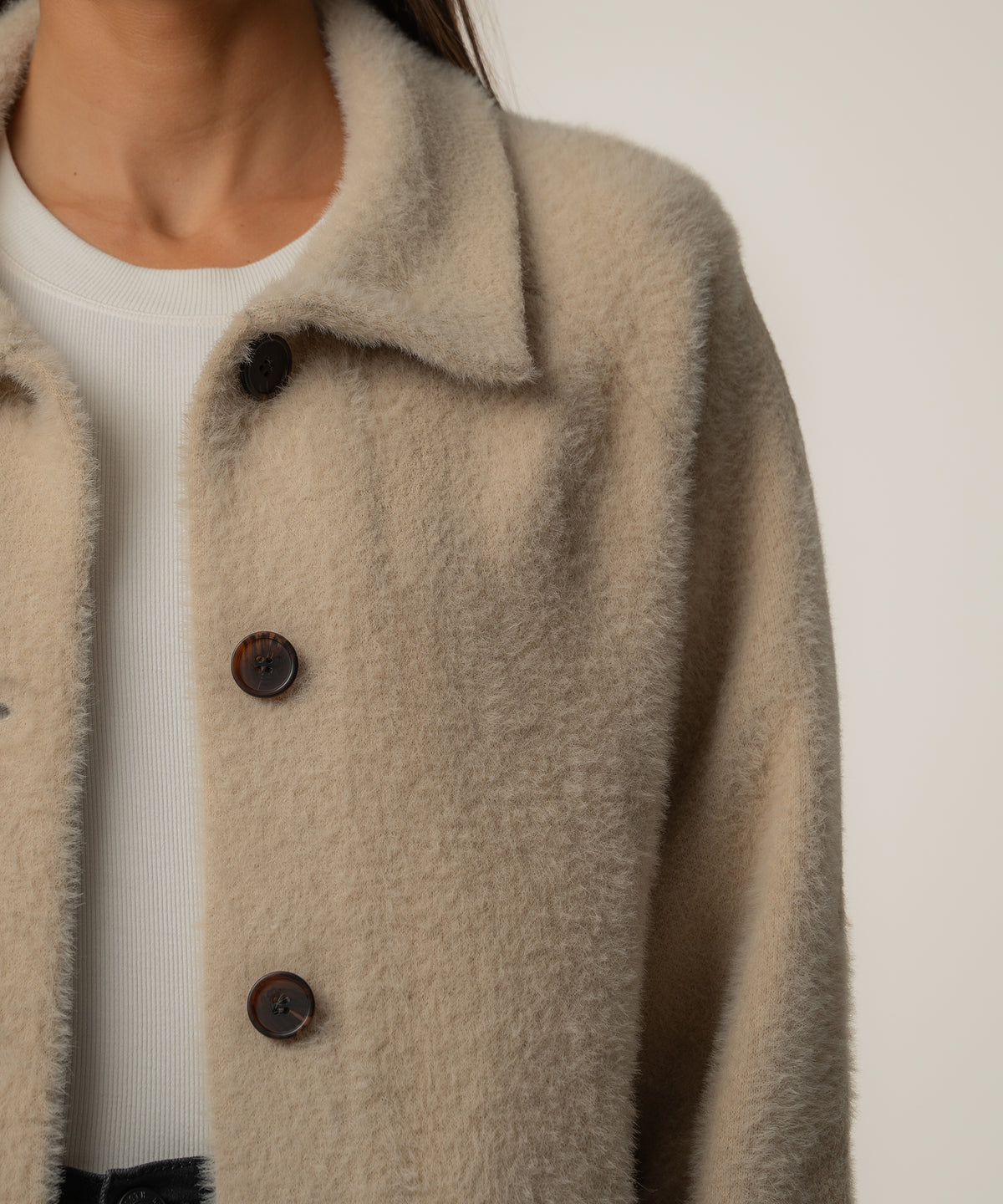 Oatmeal-colored sweater jacket with collar and dark brown buttons worn over white ribbed top.