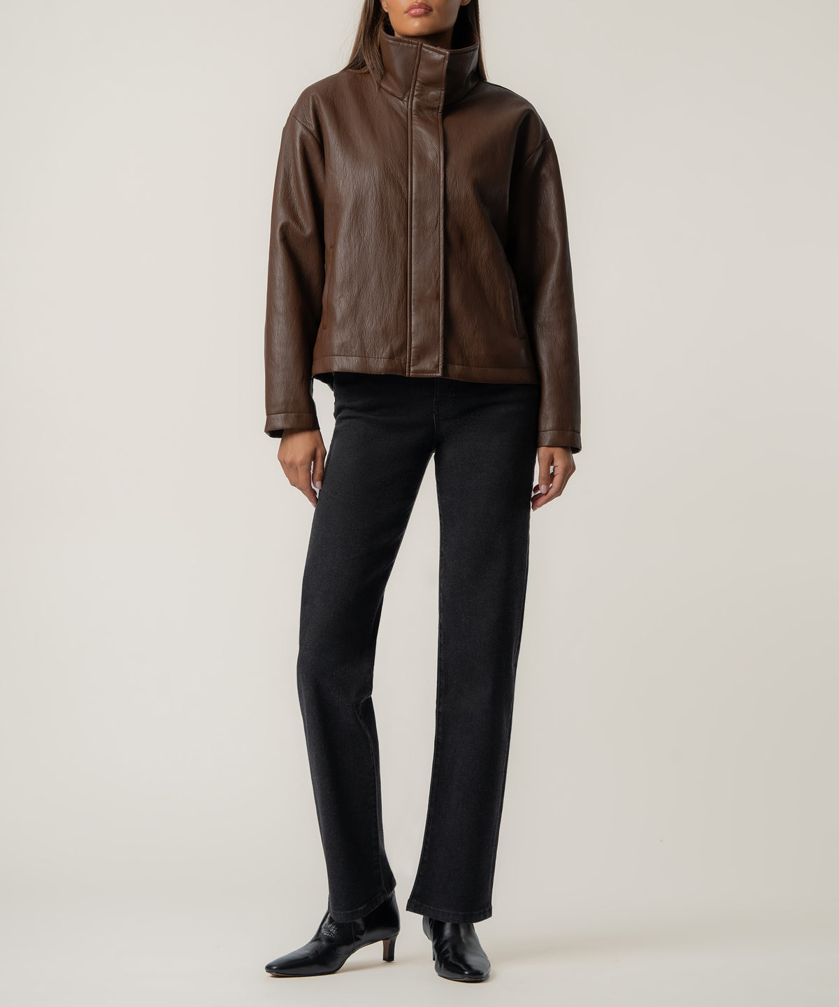 Woman wearing brown leather cropped jacket with stand collar and full-length black jeans.