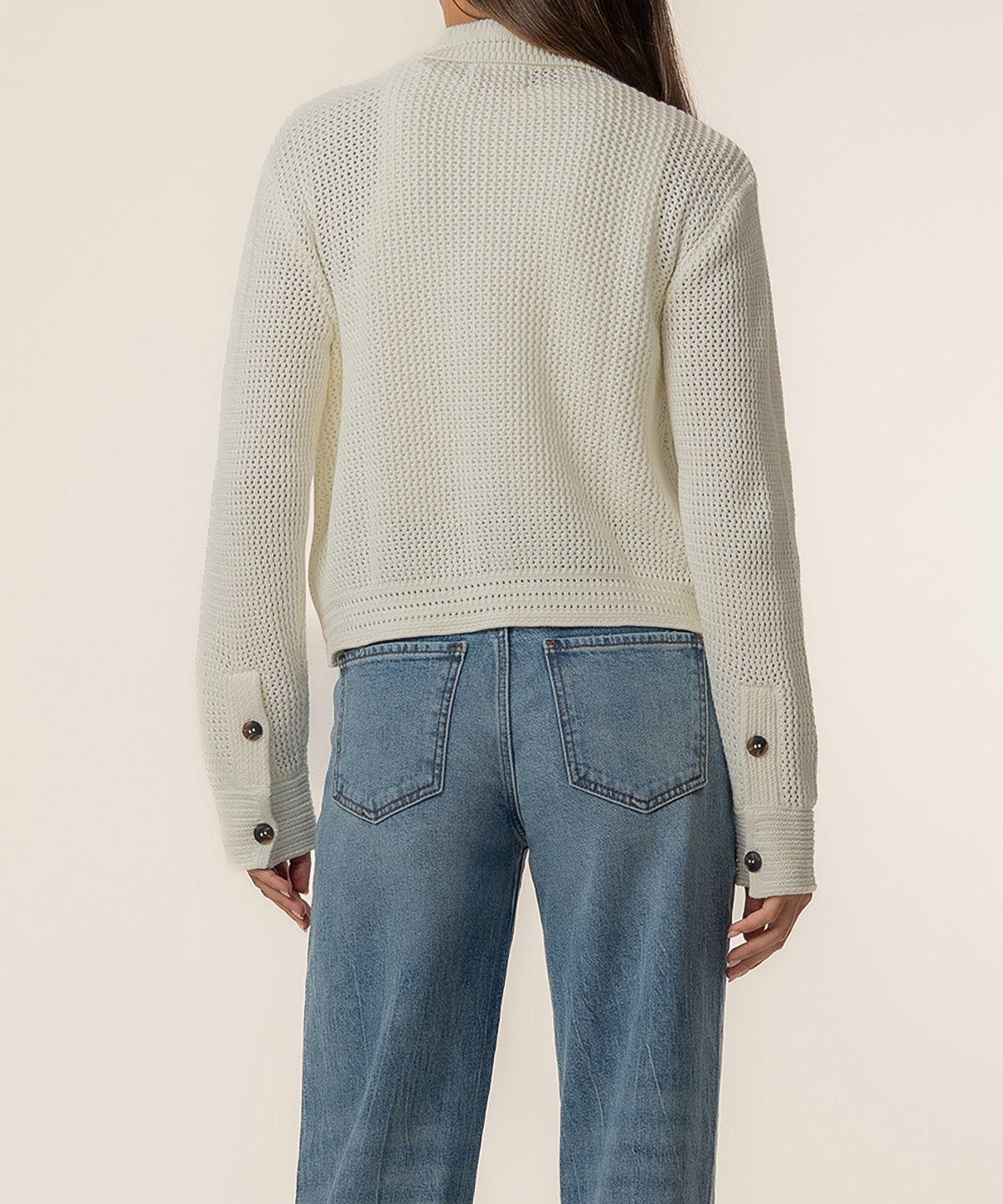 Cream knit sweater jacket with button cuffs, shown from back worn with blue jeans.