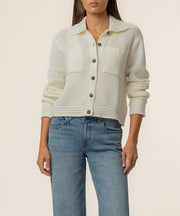 Cream knit sweater jacket with collar, button front, textured weave, and ruched sleeves worn with blue jeans.