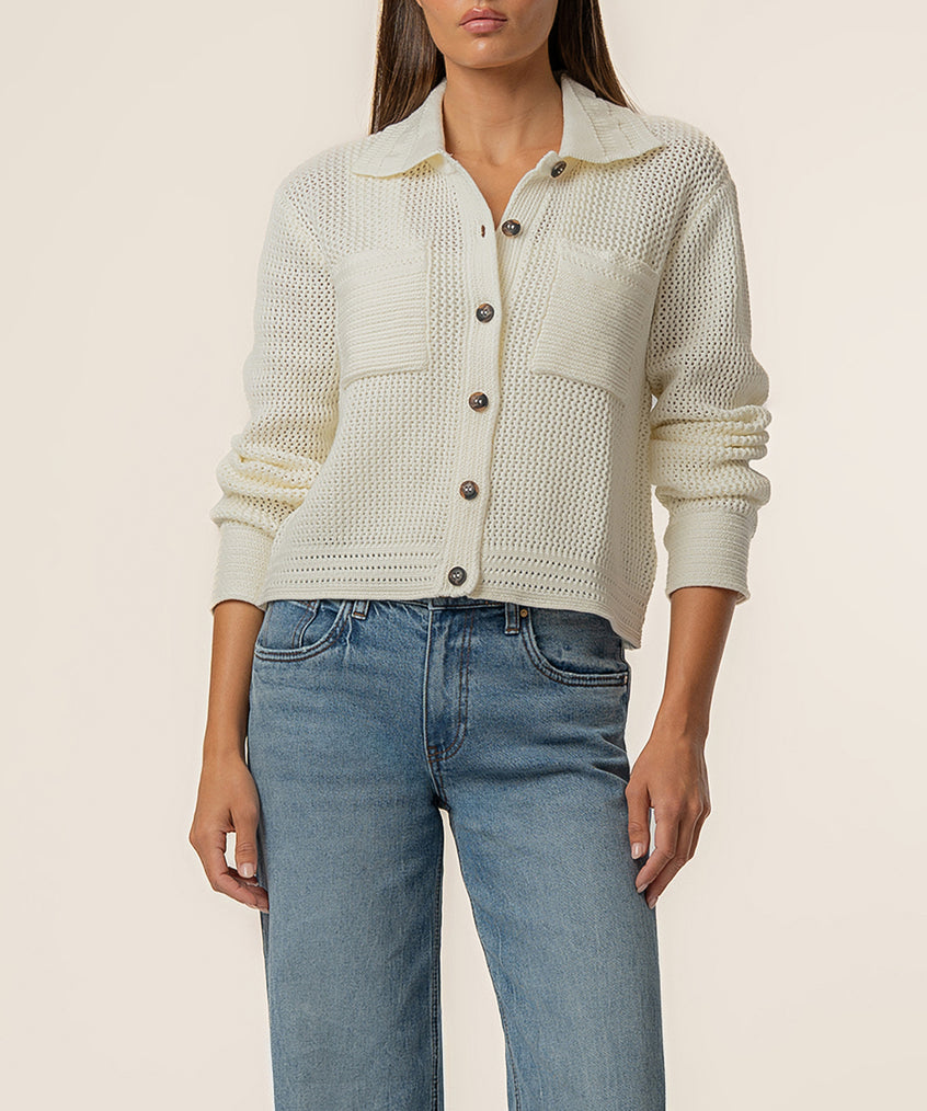 Cream knit sweater jacket with collar, button front, textured weave, and ruched sleeves worn with blue jeans.