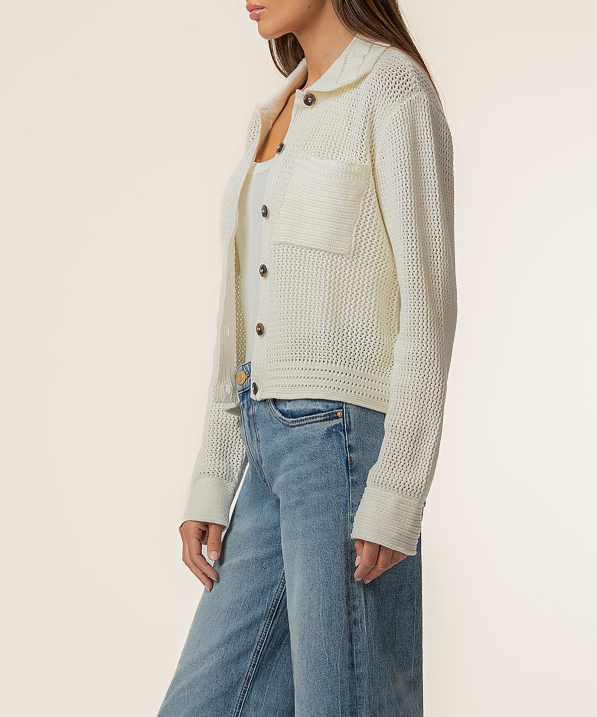 Cream knit cardigan jacket with textured pattern, button front, and ribbed cuffs worn over white top and blue jeans.