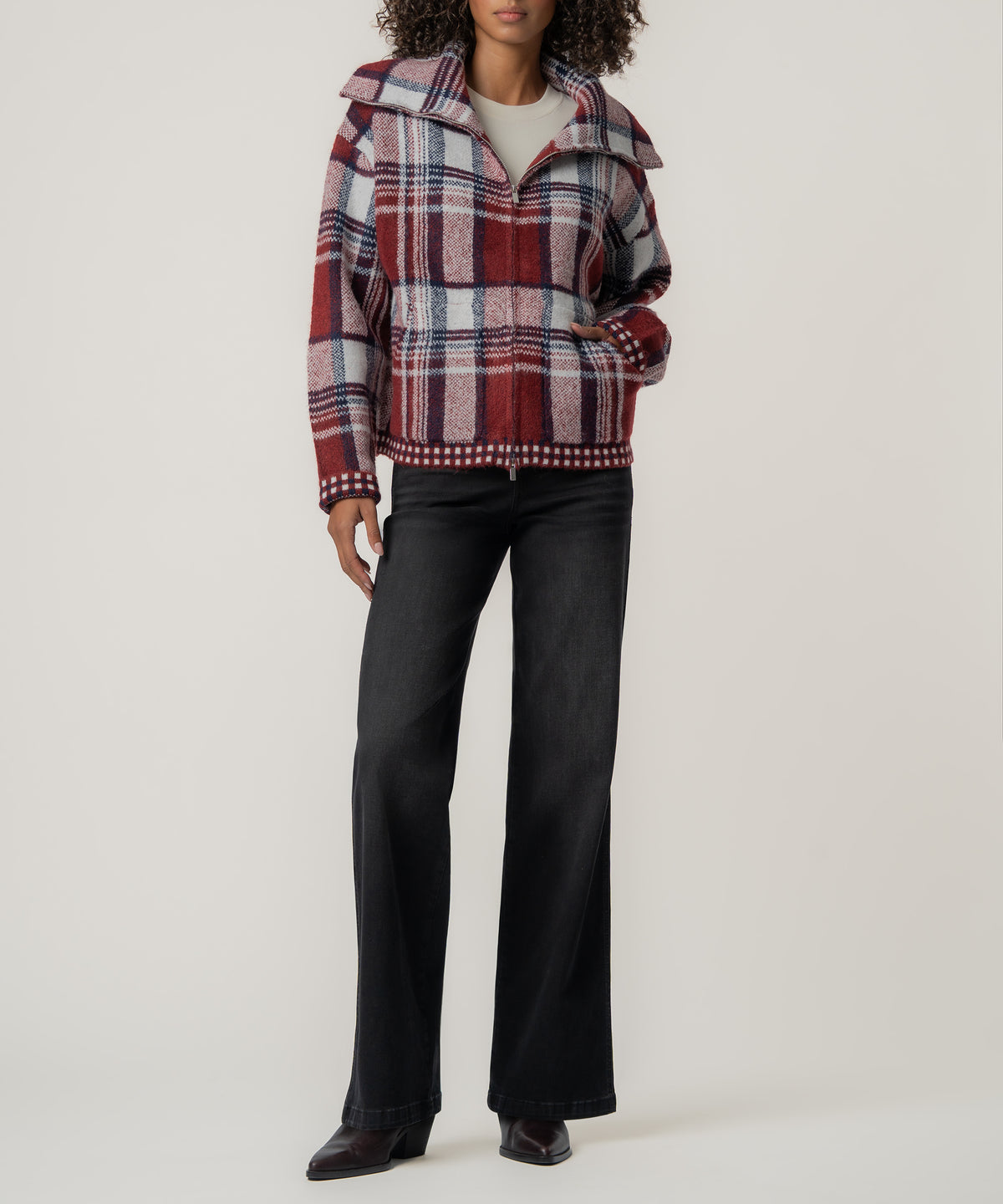 A woman wears a red, white and navy plaid zip-up knit jacket with black wide-leg jeans and dark ankle boots.