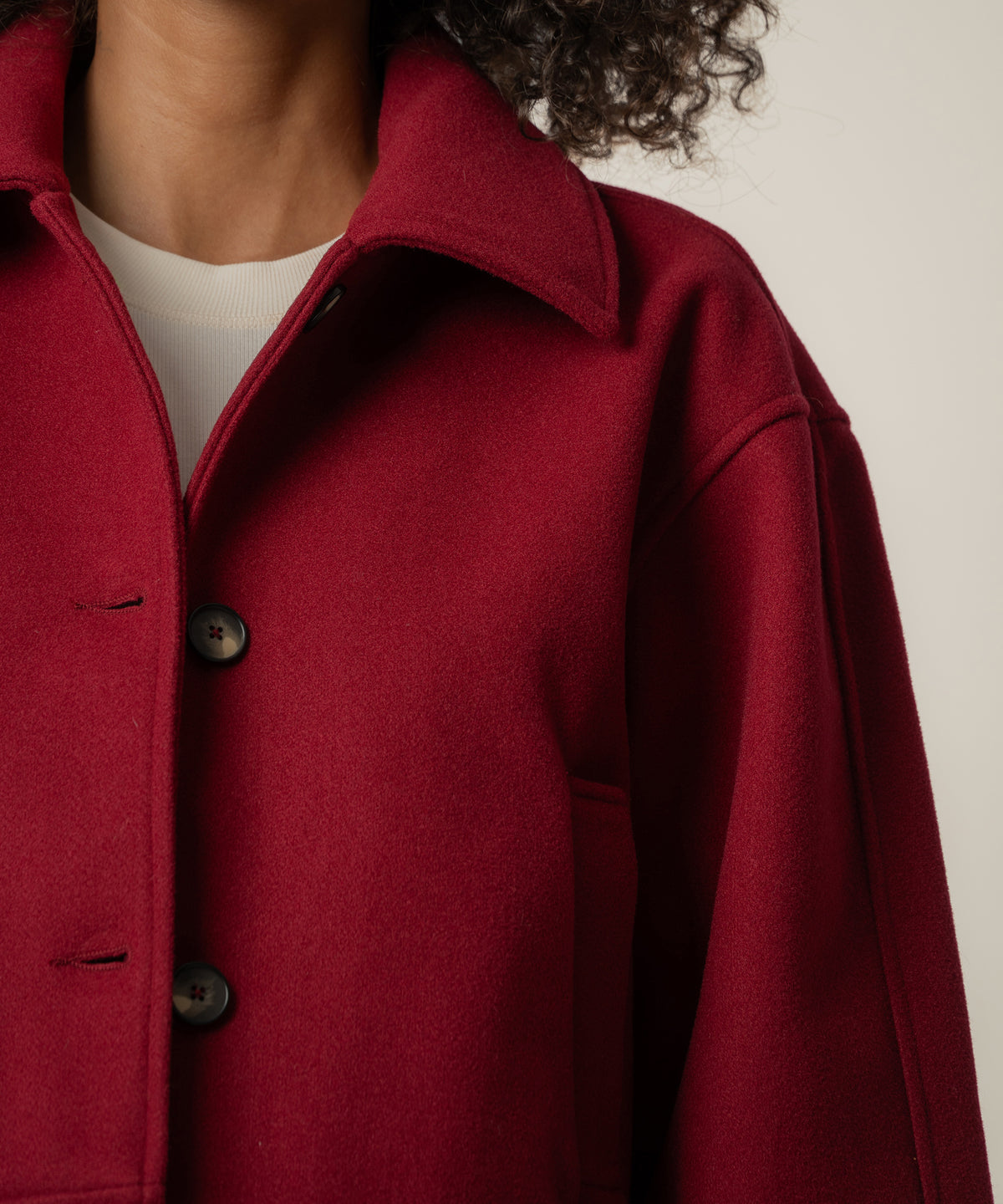 Close view of a person wearing a crimson wool-style coat with a pointed collar, dark buttons, and a cream top underneath.