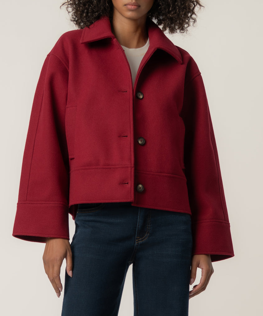 A woman wears a cropped crimson jacket with wide sleeves and three buttons over a white top and dark jeans.