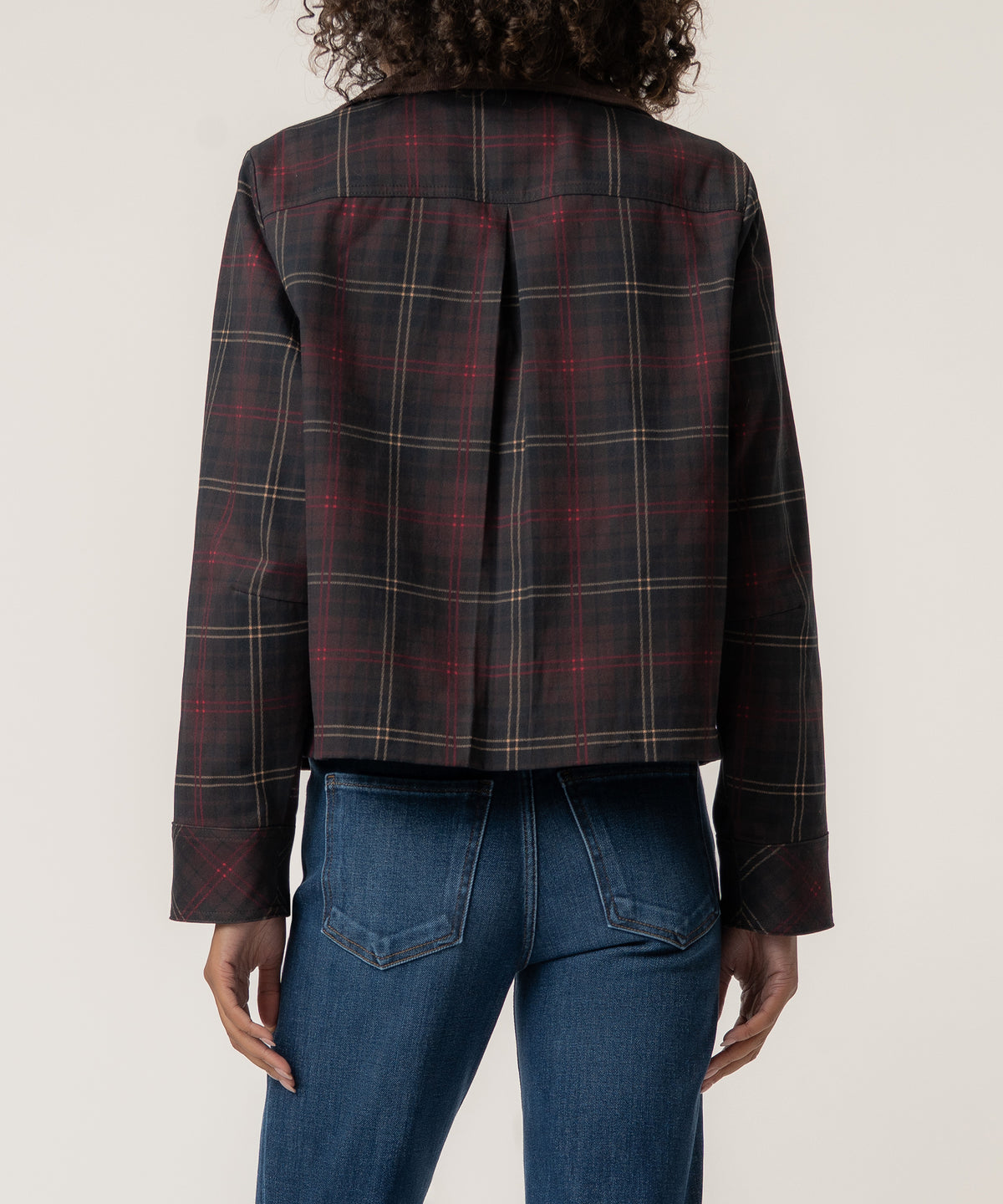 Back view of a woman wearing a cropped dark plaid jacket with red and cream stripes, a center pleat, and blue jeans.