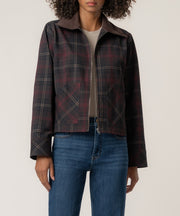 A woman wears a dark plaid zip-front jacket with a brown corduroy collar and patch pockets over blue jeans.