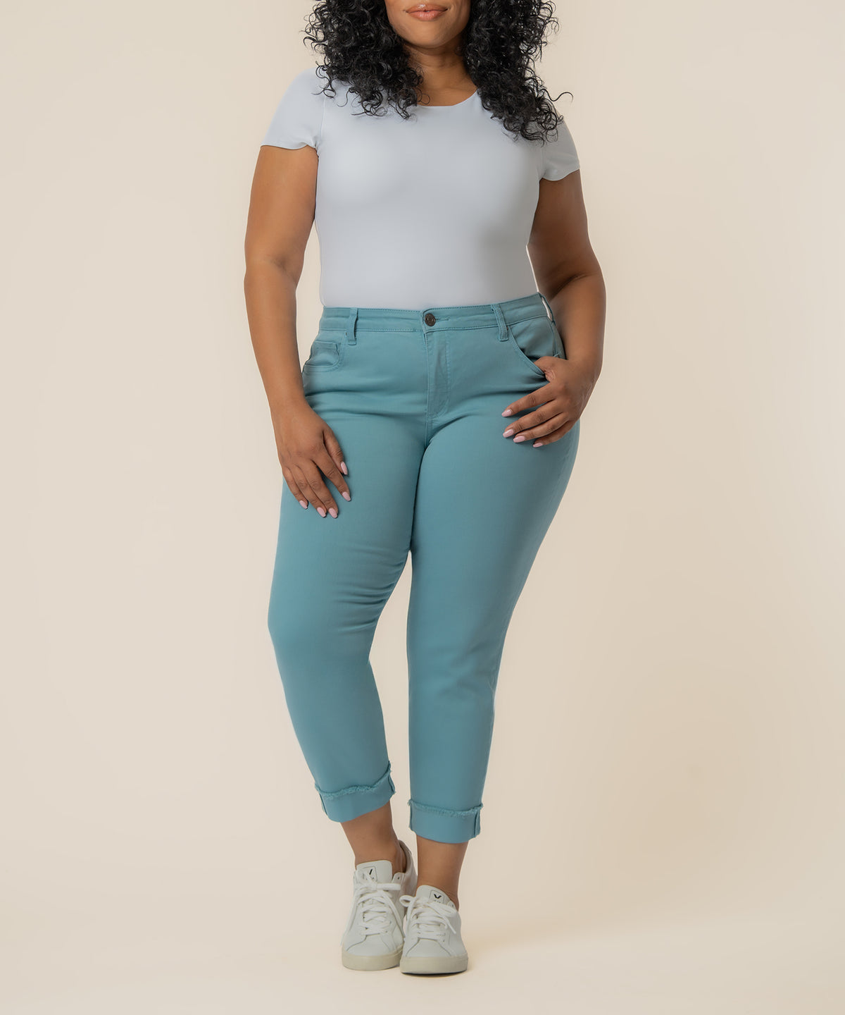Woman wearing light blue short-sleeve t-shirt and cyan cropped straight-leg jeans with rolled cuffs and white sneakers.