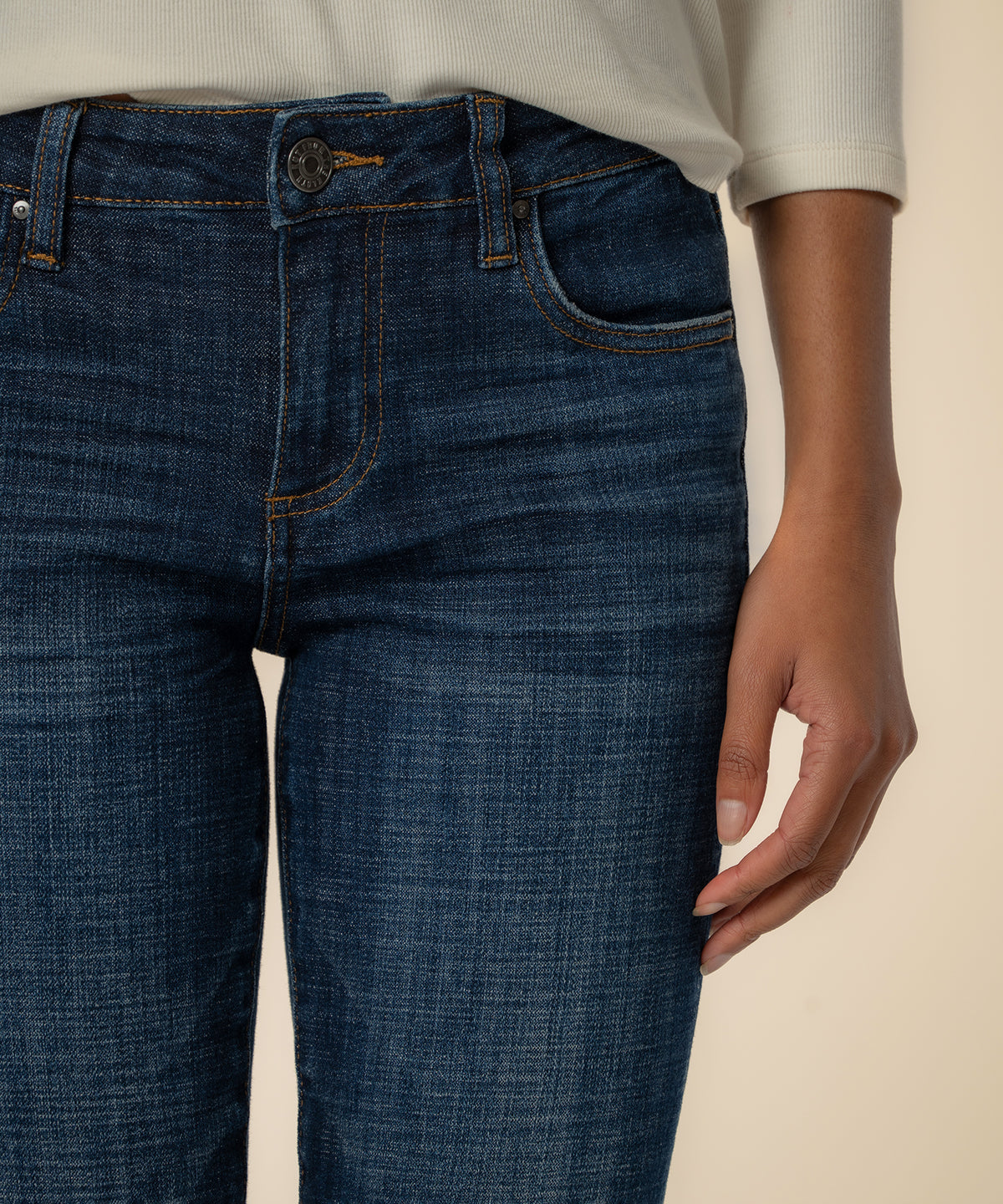 Dark blue straight-leg jeans with orange topstitching worn with a cream ribbed long-sleeve top.