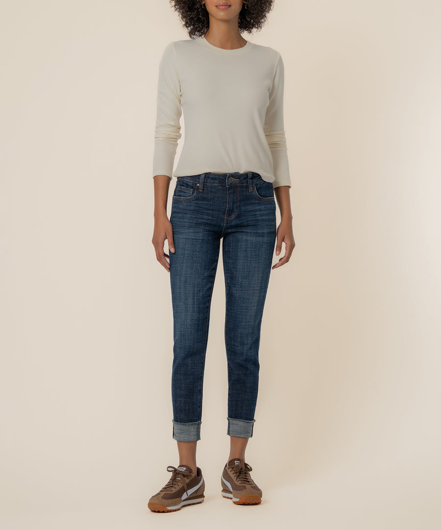 Woman wearing cream long-sleeve top and dark blue straight-leg jeans with rolled cuffs and brown sneakers.