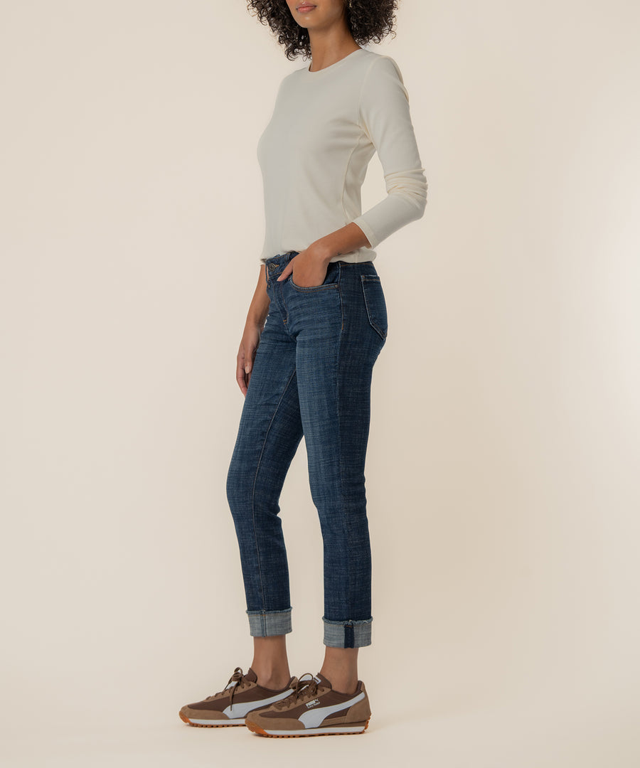 Woman wearing cream long-sleeve shirt tucked into dark blue straight-leg jeans with cuffed ankles.