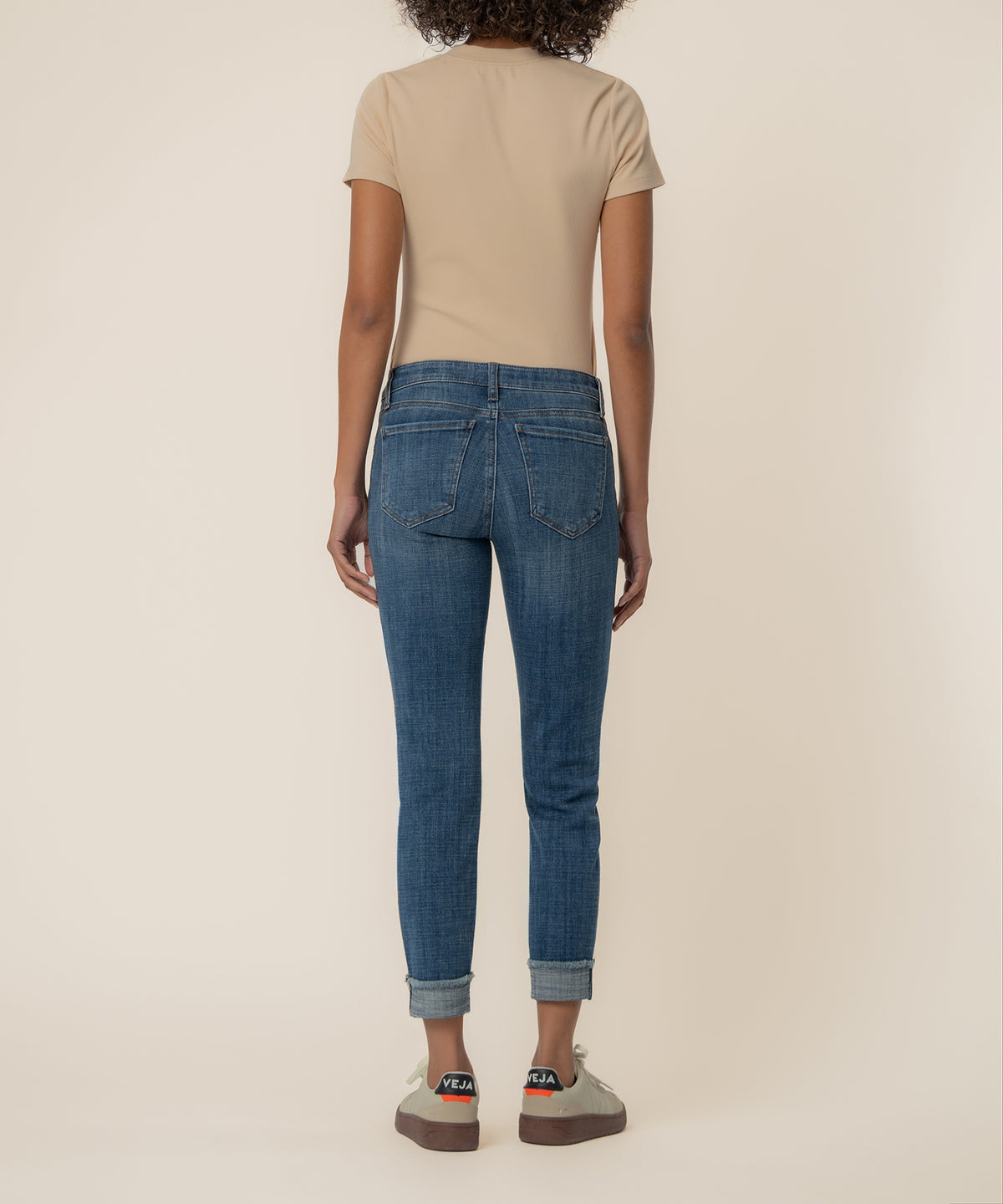 Woman wearing mid-rise blue cropped straight leg jeans with cuffed ankles and a beige t-shirt, shown from behind.