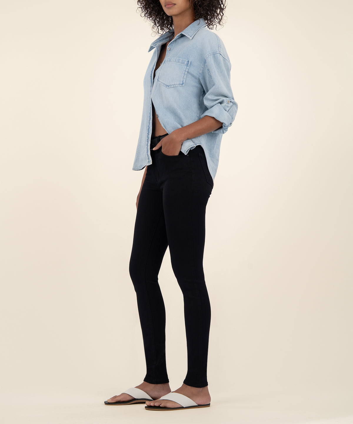 Woman wearing black high-rise skinny jeans with light blue denim shirt and slide sandals.