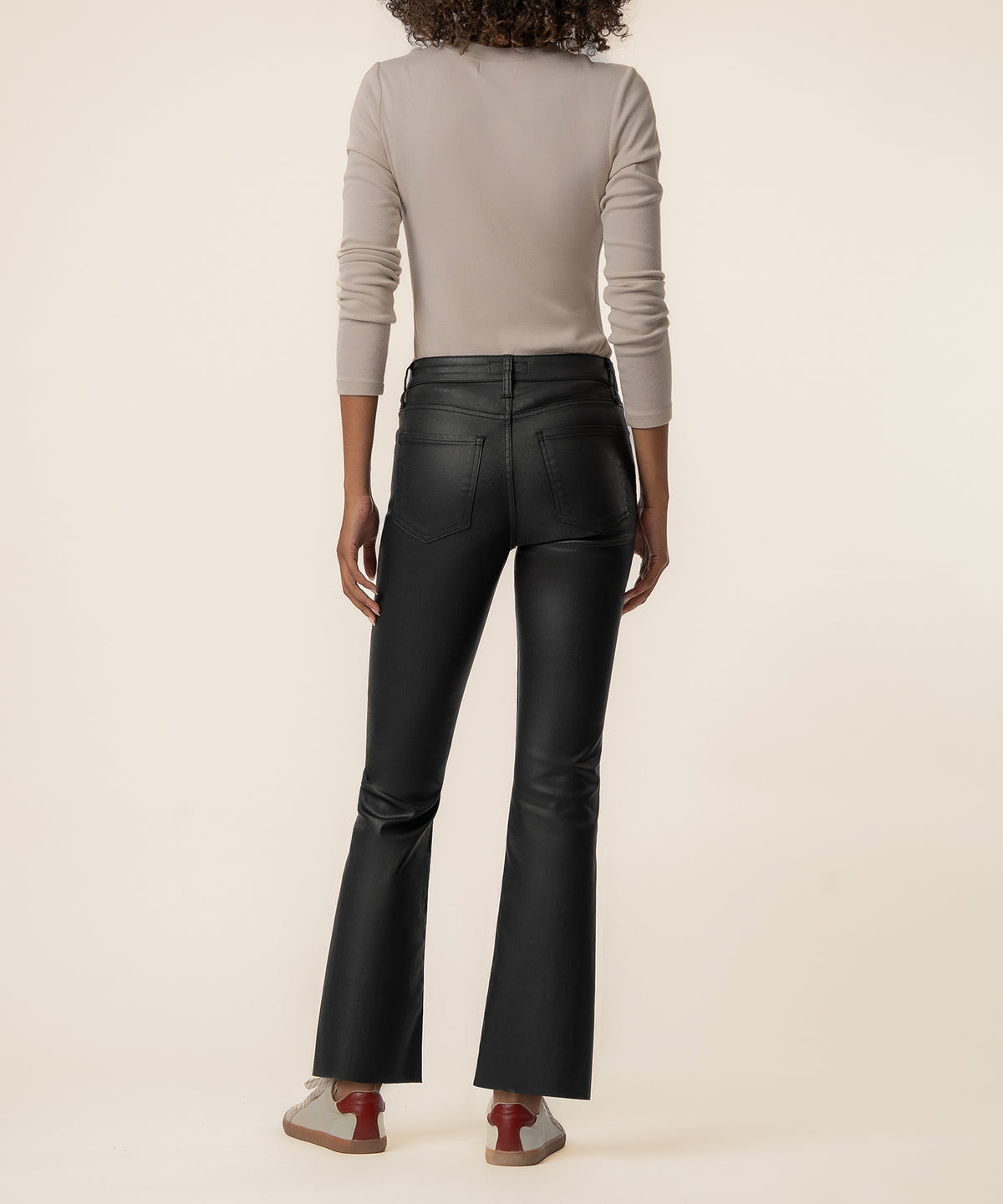 Black coated high-rise ankle flare jeans with a glossy finish, shown from back view on a model wearing a beige long-sleeve to