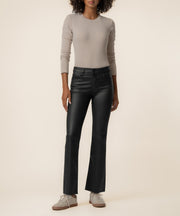 Woman wearing black coated high-rise ankle flare pants with cream long-sleeve top and white lace-up shoes.