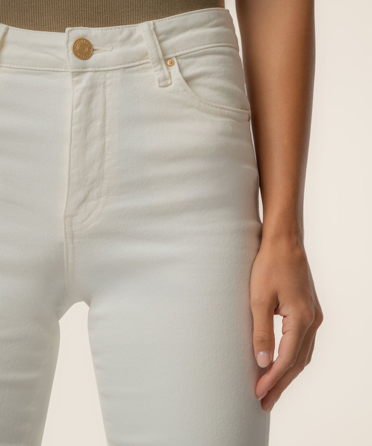 Cream-colored high-rise ankle flare jeans with gold button and zipper detail at waistband.