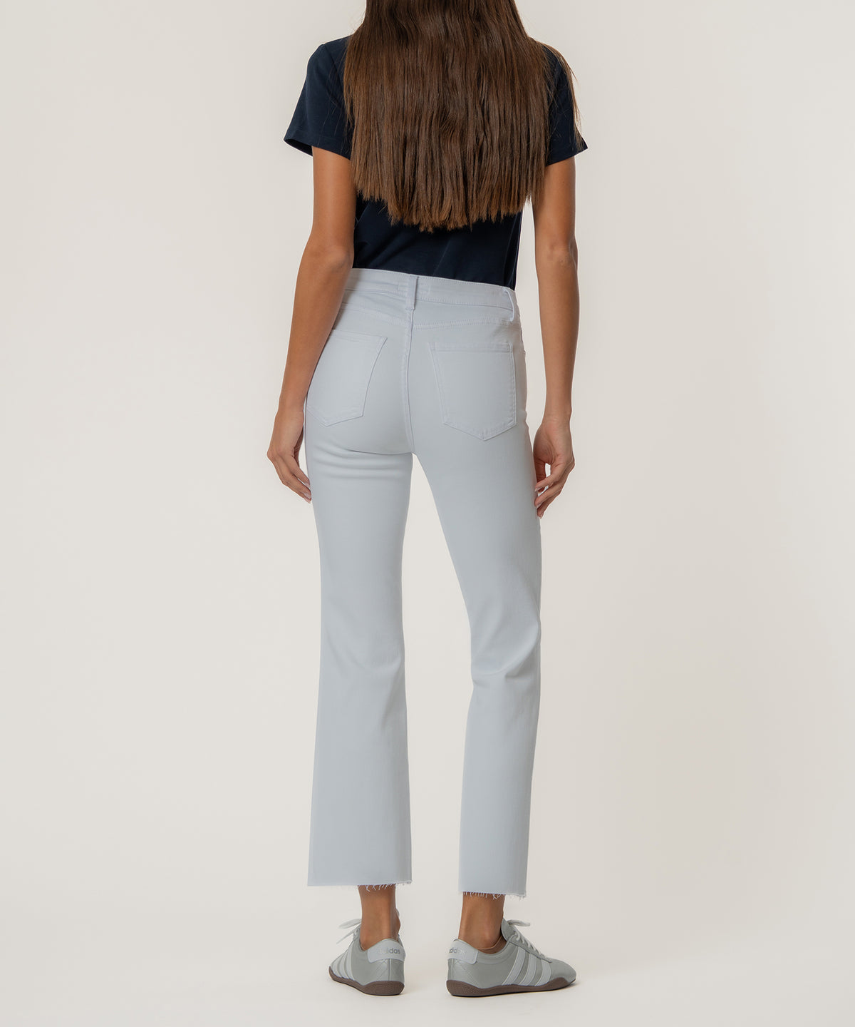 White high-rise ankle flare jeans with raw hem, shown from back on model wearing navy top.