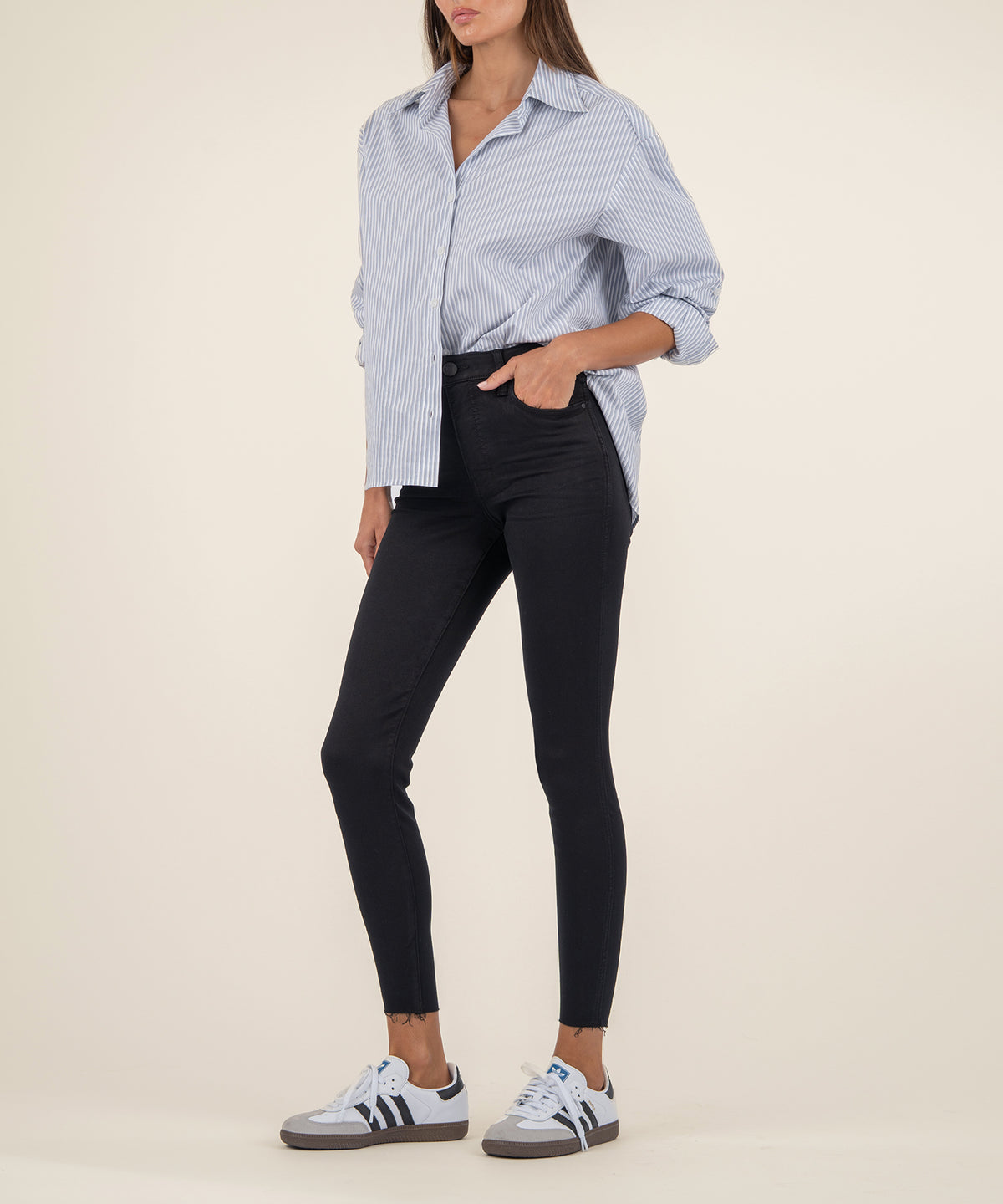 Black high-rise ankle skinny jeans with a cropped raw hem, styled with a blue striped button-up shirt.