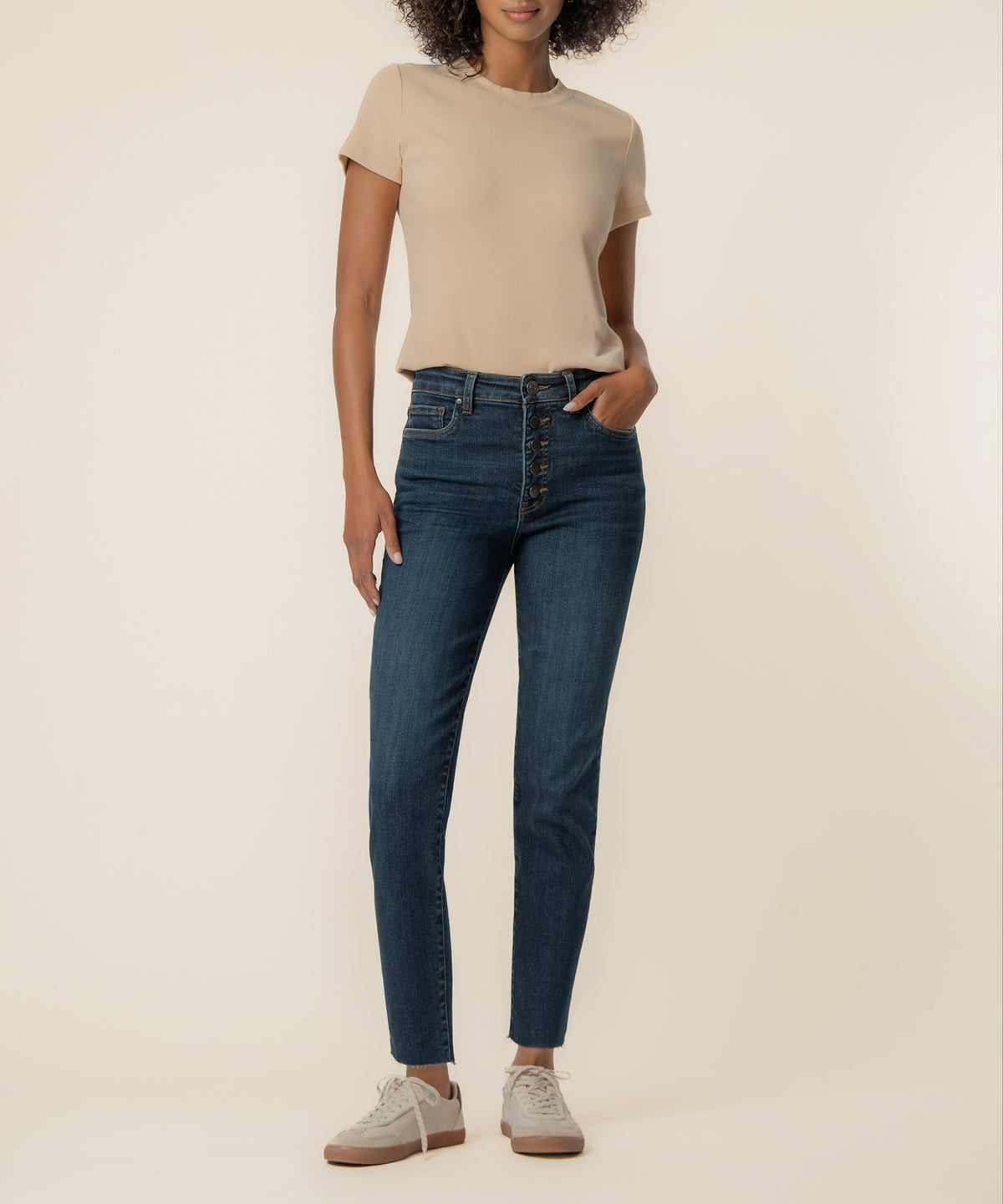 Woman wearing high-rise dark blue jeans with button fly and beige short-sleeve t-shirt.