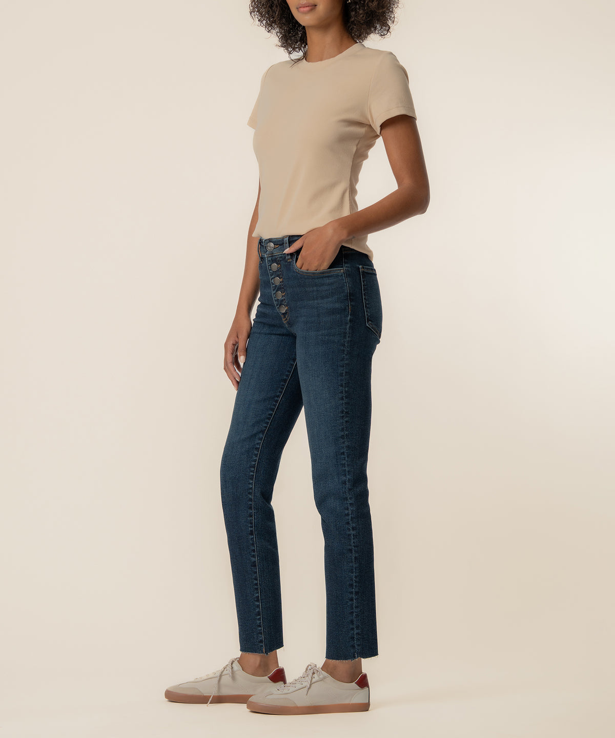 Woman wearing high-rise dark blue mom jeans with button fly and a beige short-sleeve t-shirt.