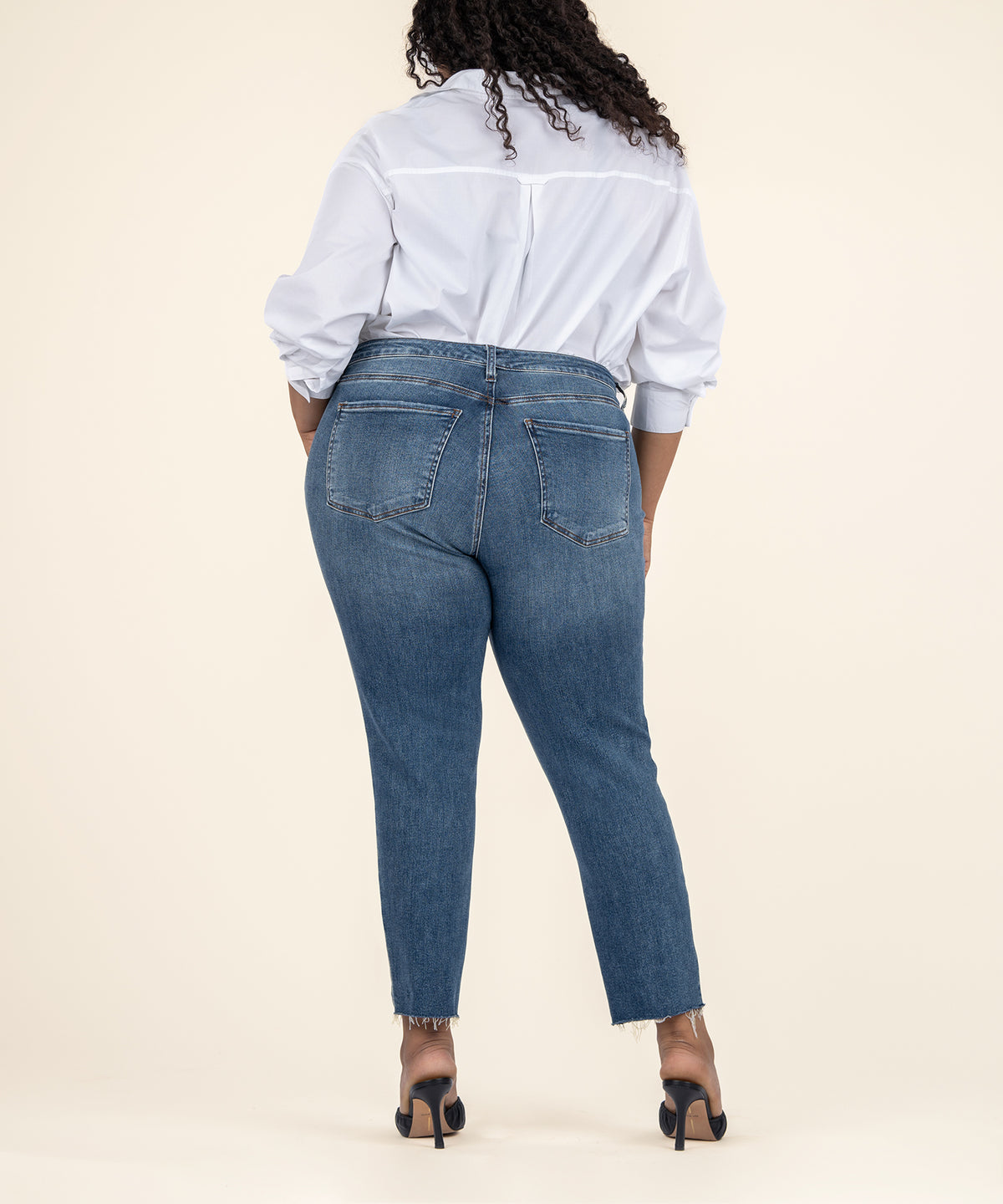 Woman wearing white button-up shirt and medium wash straight-leg ankle jeans with frayed hem, shown from behind.