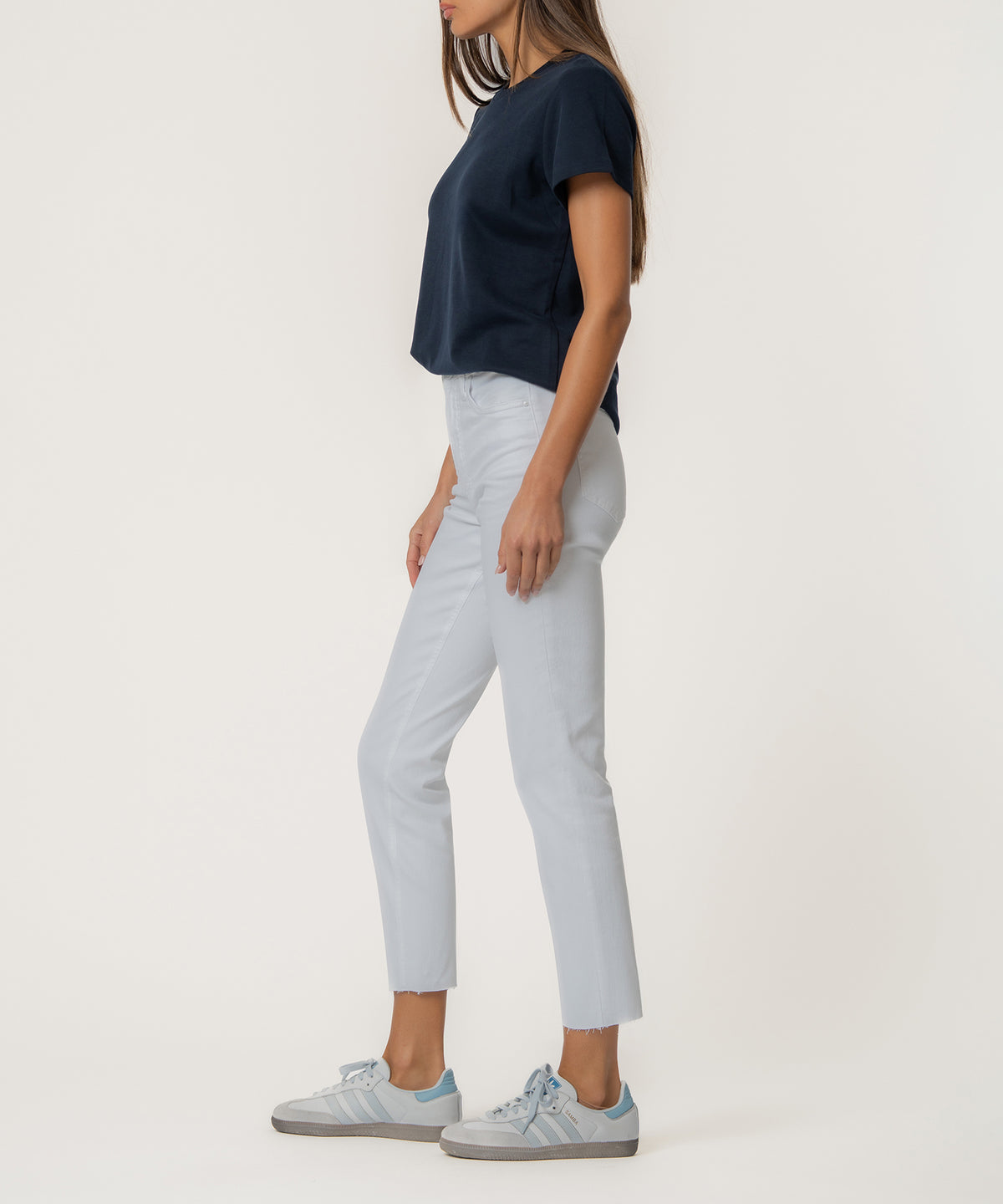 Woman wearing light optic white high-rise mom jeans with a navy t-shirt and sneakers, shown from the side.