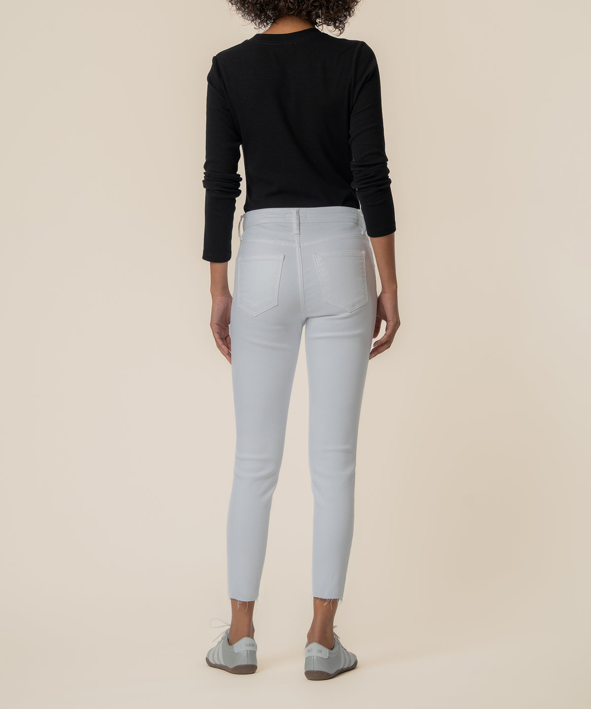 Woman wearing white high-rise cropped jeans with five-pocket styling and distressed ankle cuffs, shown from behind.