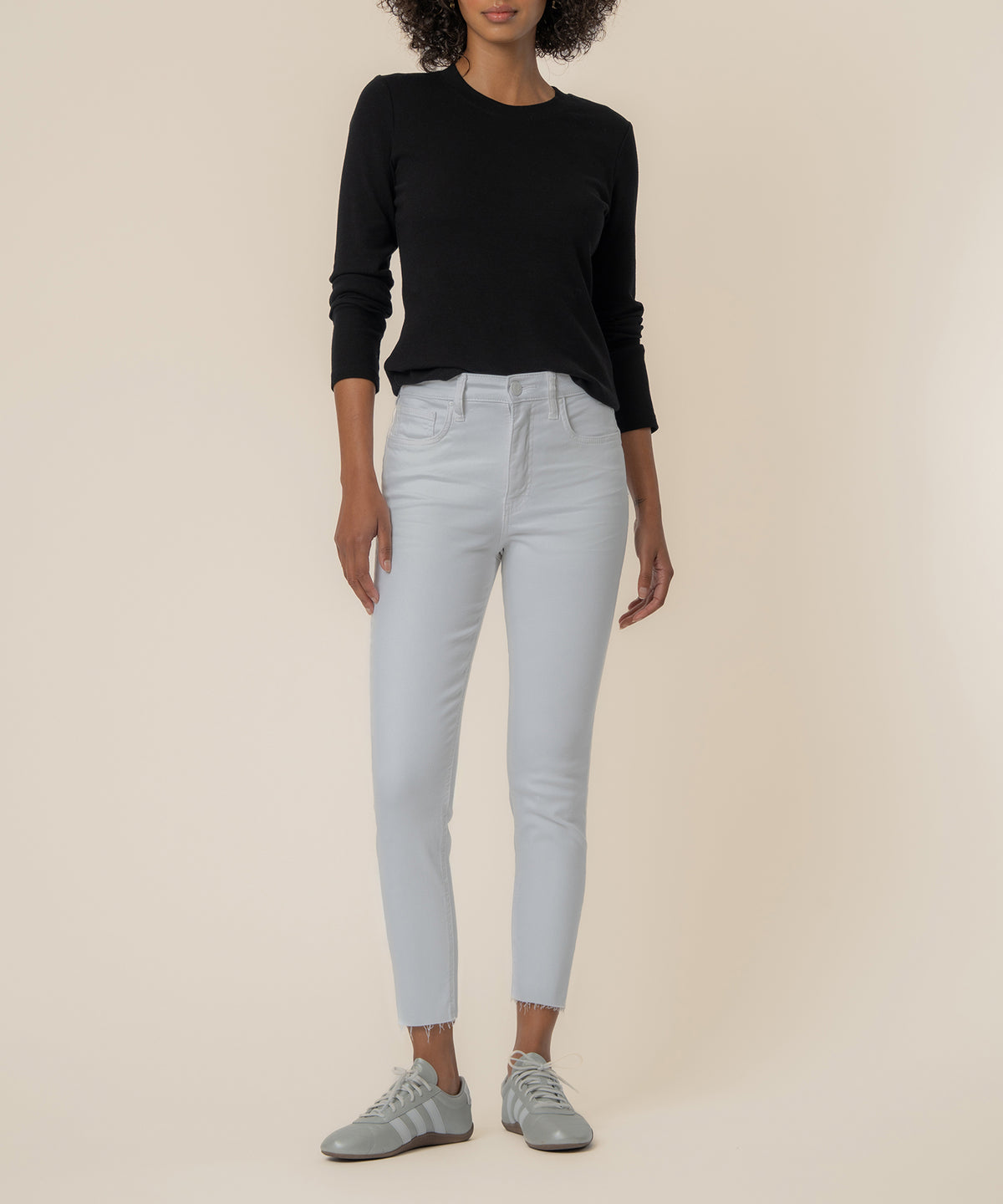 Woman wearing black long-sleeve top and high-rise white mom jeans with frayed ankle hem and gray sneakers.