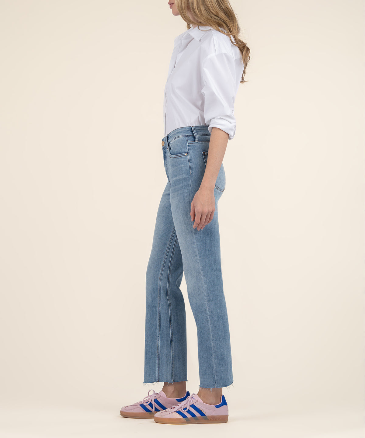 Woman wearing light blue high-rise ankle flare jeans with white button-up shirt and sneakers, shown from side view.