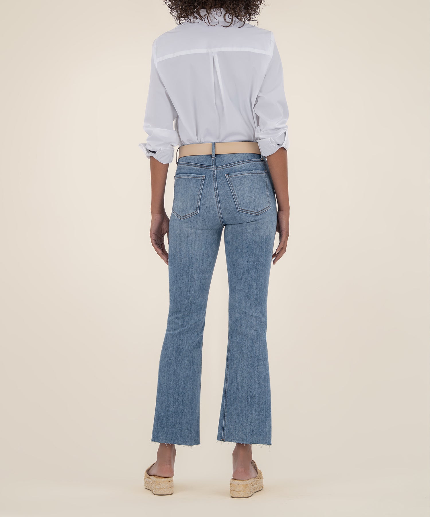 Light wash high-rise ankle flare jeans with frayed hem, shown from back on model wearing white button-up shirt.