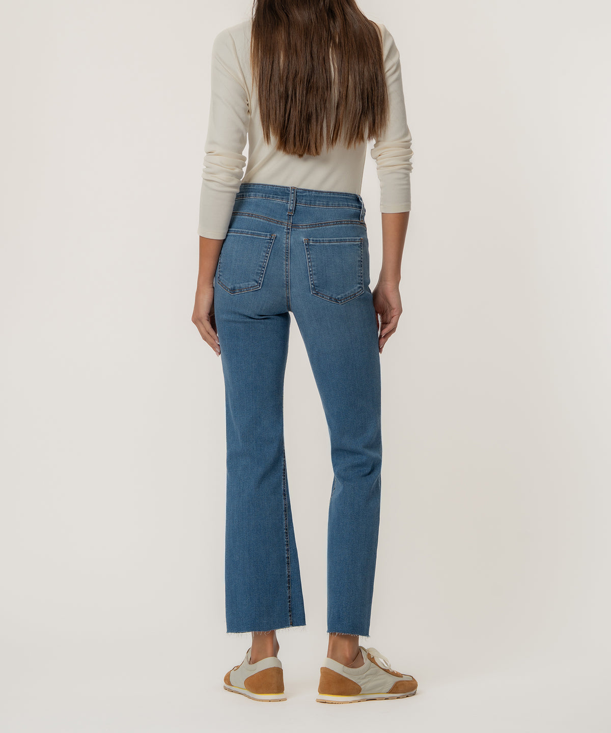Woman wearing high-rise medium-wash flare jeans with ankle-length flared hem and raw edges.