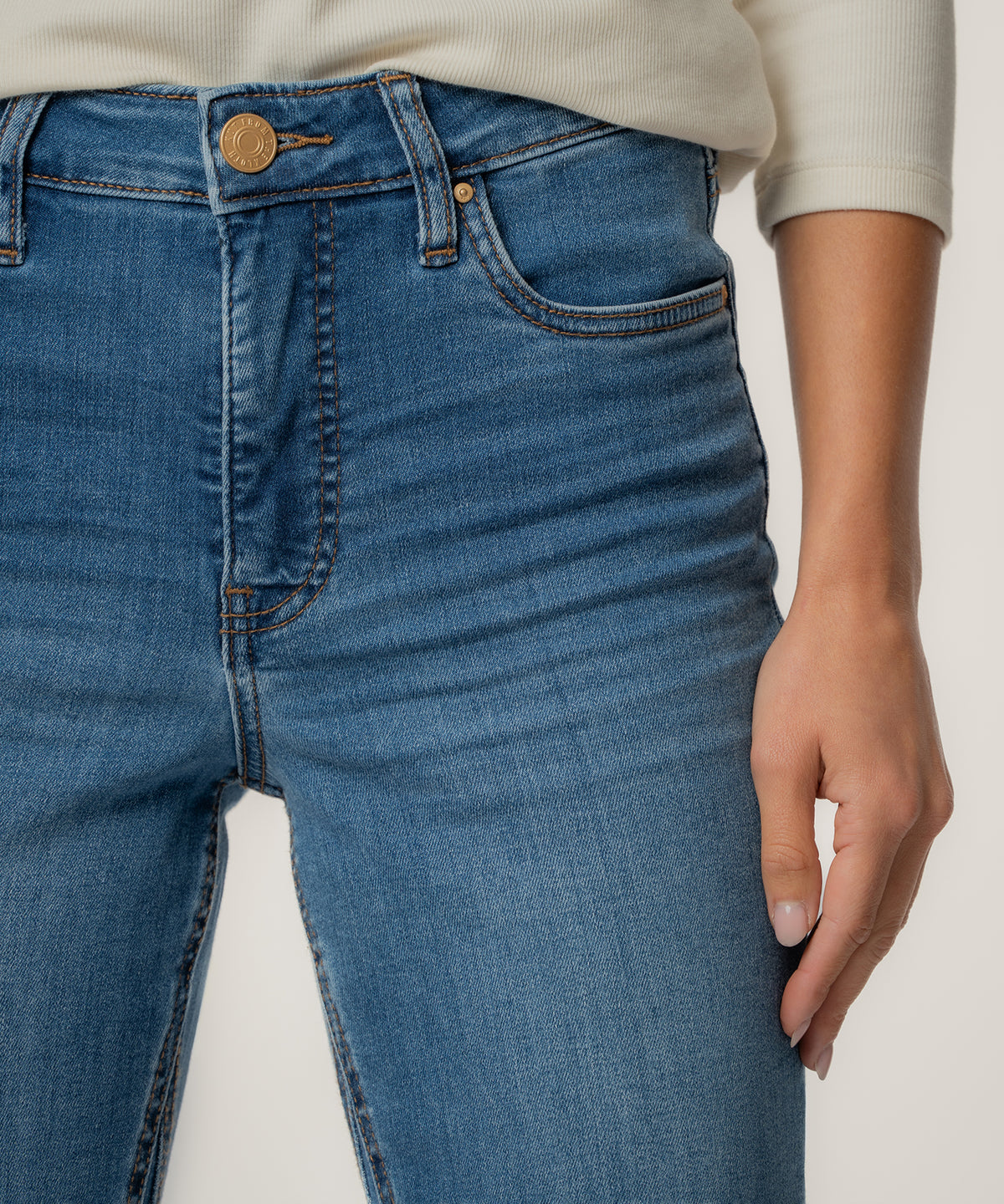 Medium-wash high-rise jeans with flared ankle, gold button closure, and five-pocket styling shown on model.