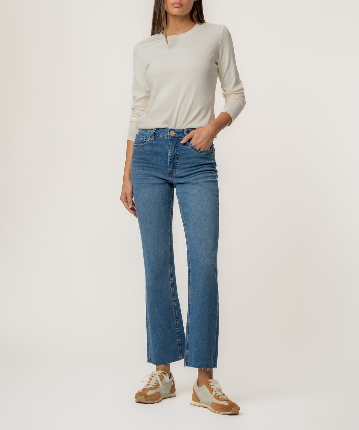 Woman wearing high-rise medium wash ankle flare jeans with a cream long-sleeve top and tan sneakers.