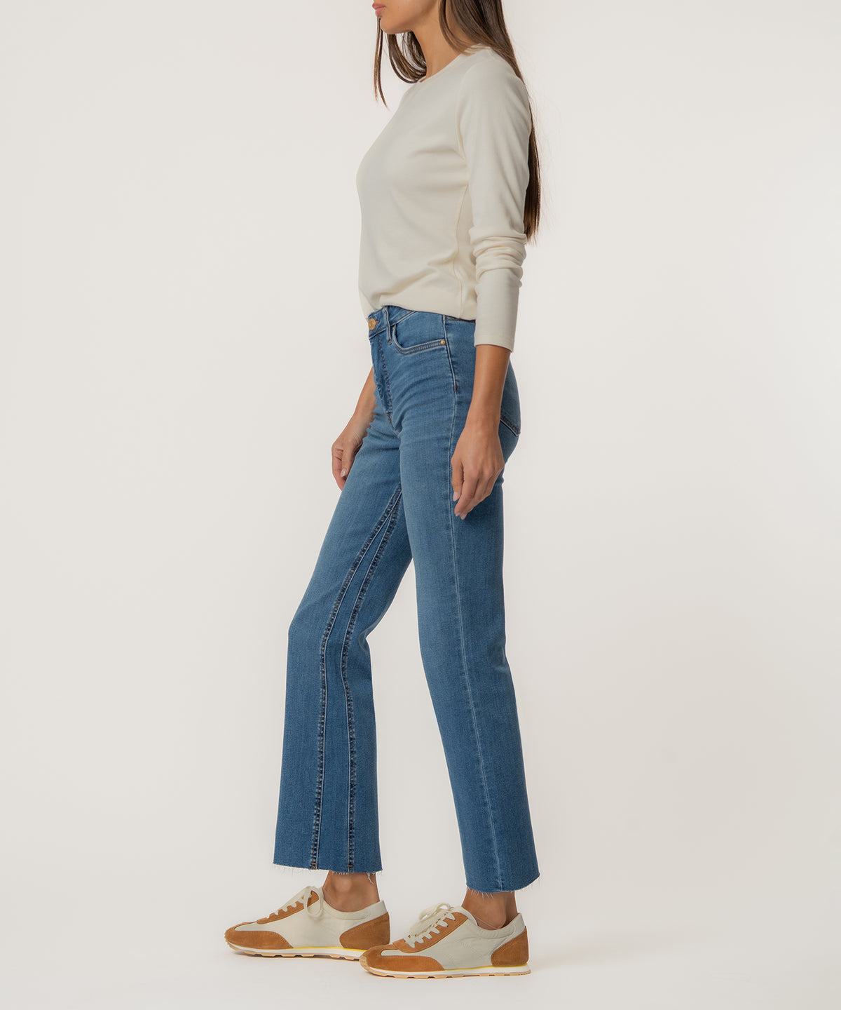 Woman wearing high-rise blue ankle flare jeans with cream long-sleeve top and tan sneakers.