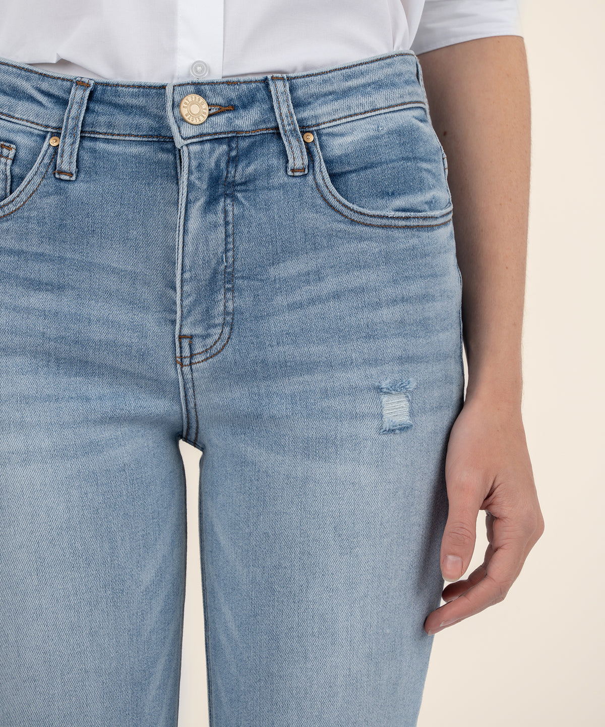 Light wash high-rise mom jeans with distressed detail on thigh, worn with white button-up shirt.