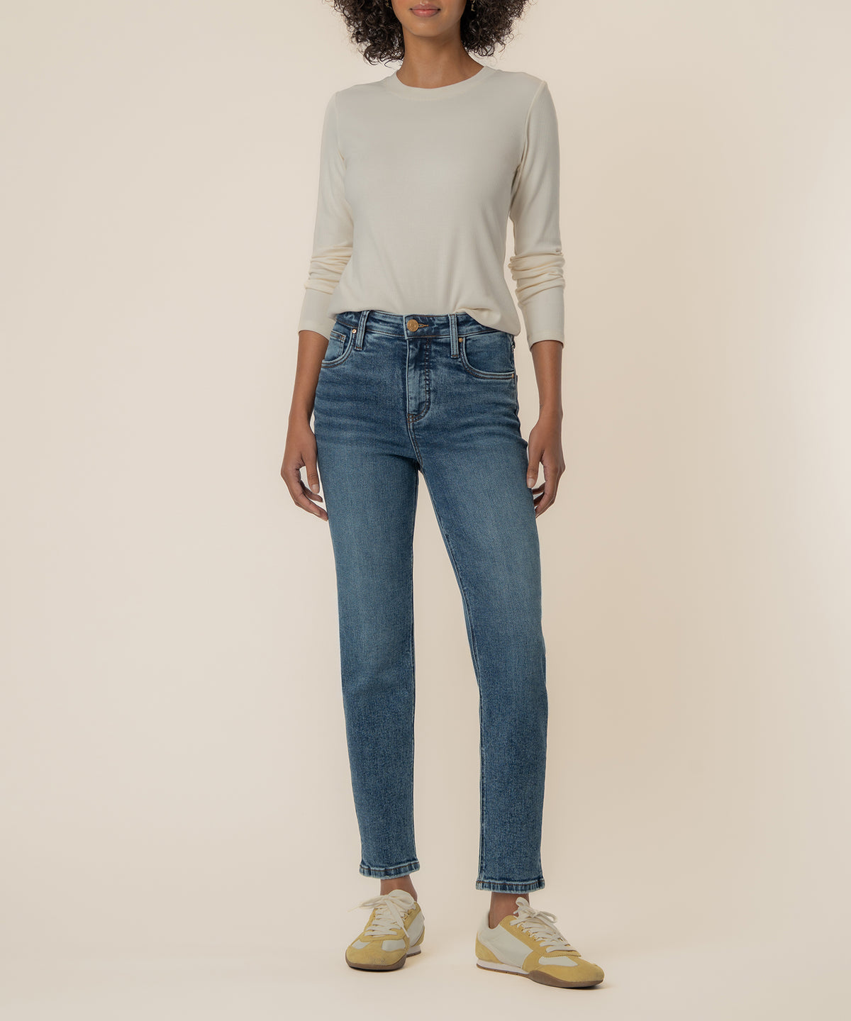 Woman wearing high-rise medium-wash straight-leg jeans with a cream long-sleeve top and yellow sneakers.