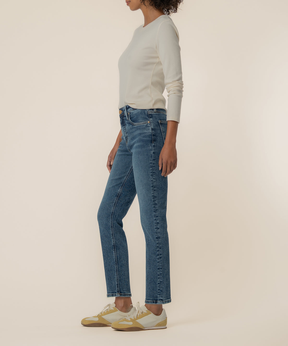 Woman wearing cream long-sleeve top and medium-wash high-rise straight-leg jeans with white and yellow sneakers.