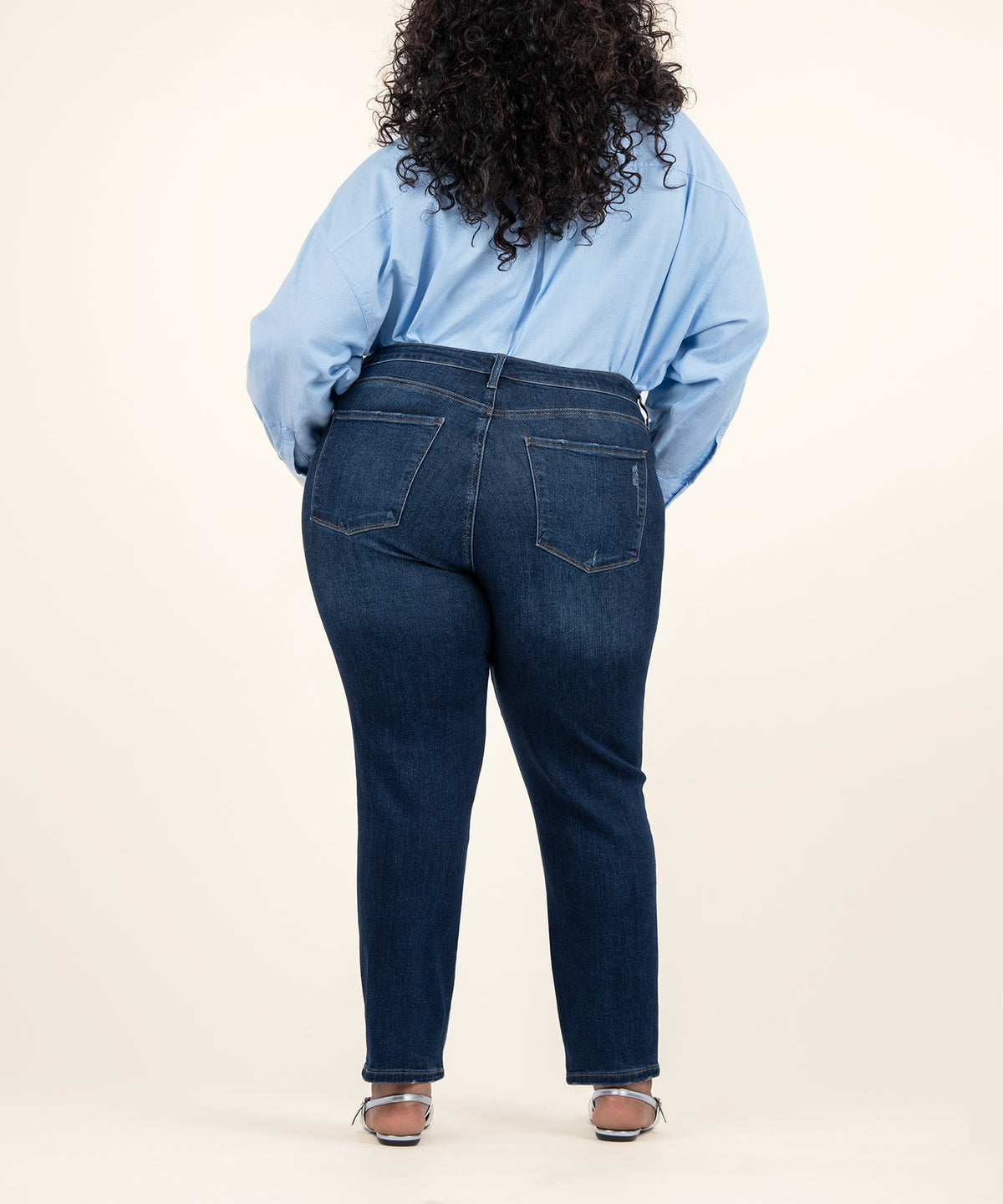 Dark blue high-rise straight leg jeans with ankle length, shown from back view on model wearing light blue shirt.