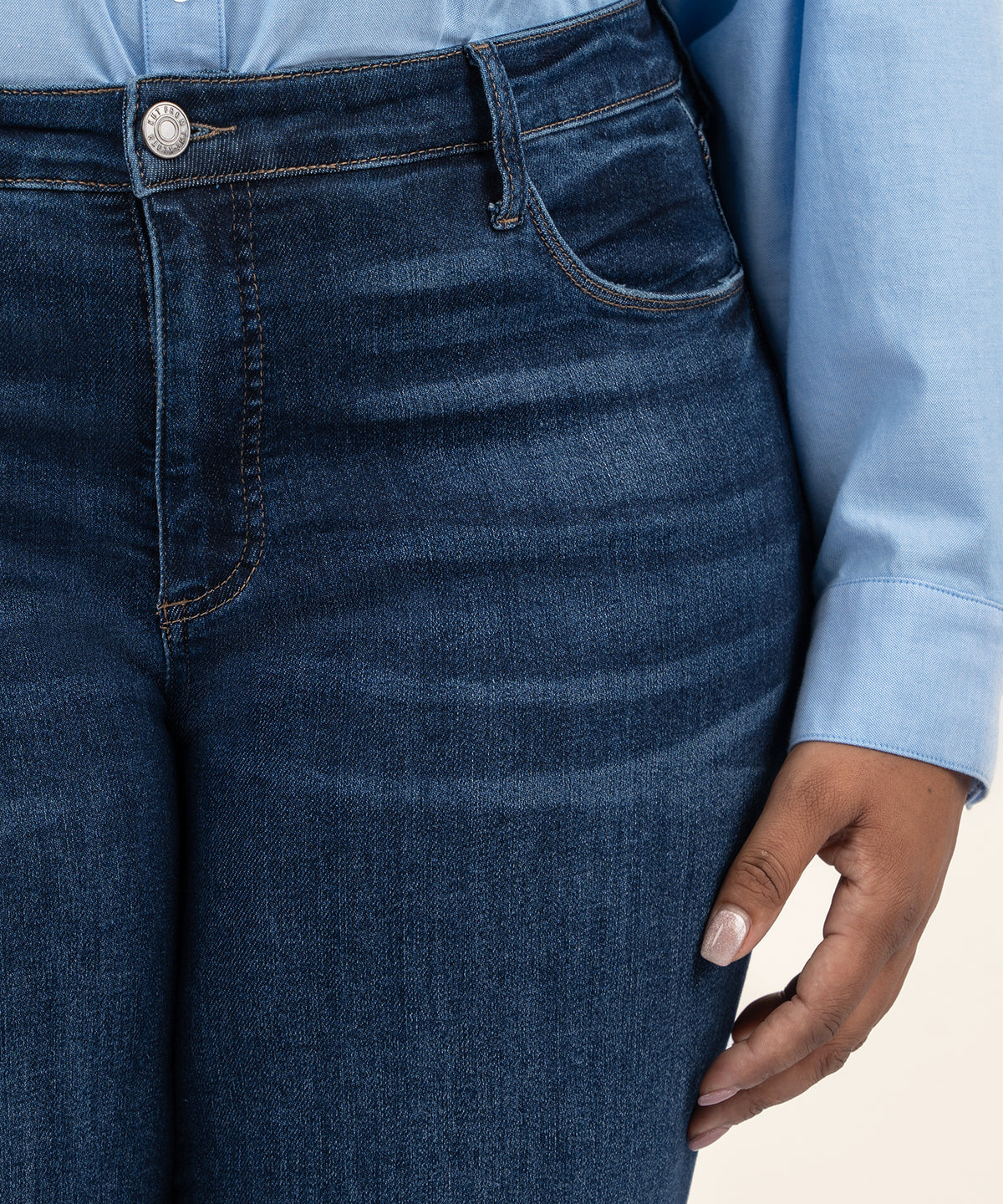 Dark wash straight leg jeans with high rise waistband and silver button detail, worn with light blue shirt.