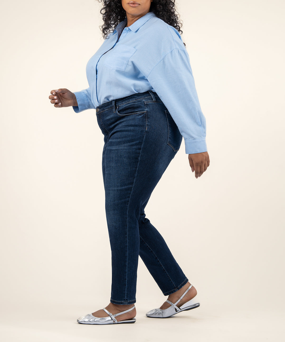 Woman wearing light blue button-up shirt and dark blue high-rise straight leg jeans with silver flat sandals.